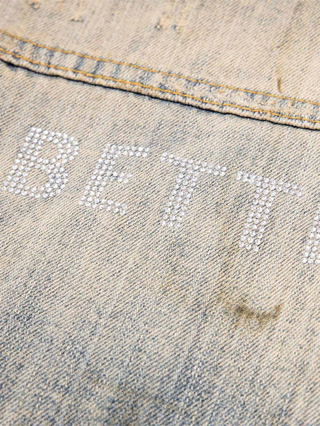 A detailed view of rhinestone embellishment on mud-dyed distressed denim by TALISHKO.