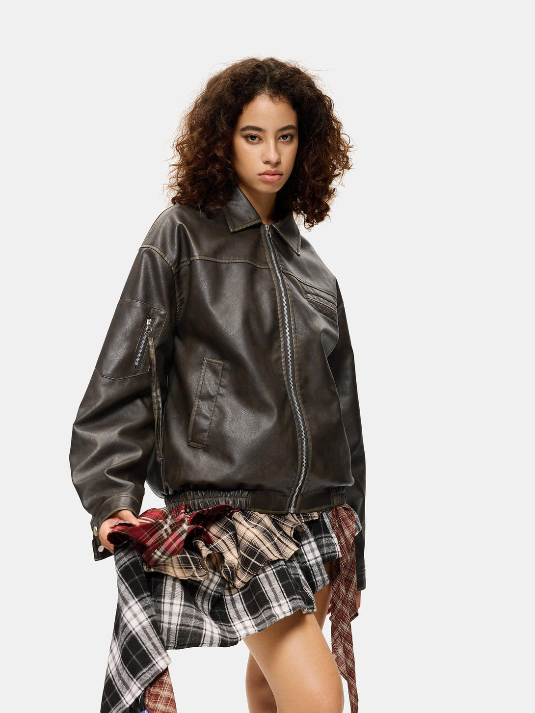 Model wearing a TALISHKO faux leather jacket with a plaid skirt, highlighting a chic style.