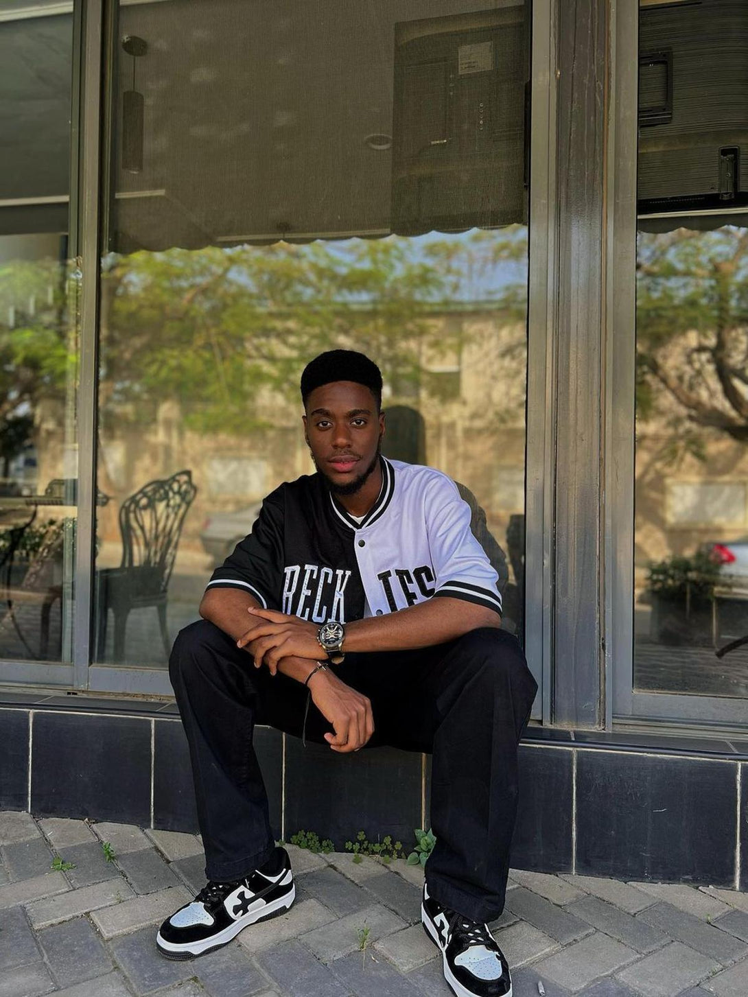 Model sitting in black and white TALISHKO casual shoes, capturing a trendy streetwear vibe.