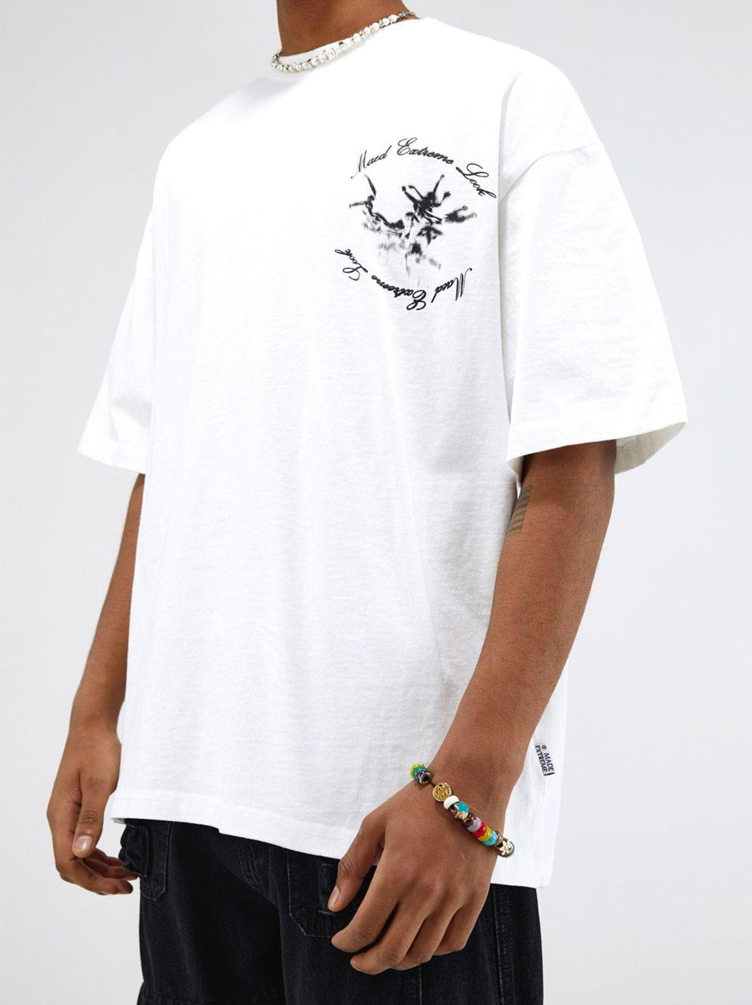 Model wearing TALISHKO white graphic tee with artistic monster design and colorful bracelet.