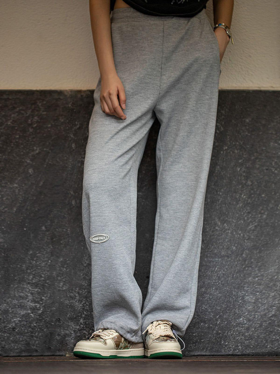 Model wearing gray TALISHKO sweatpants paired with unique skate shoes in a casual setting.