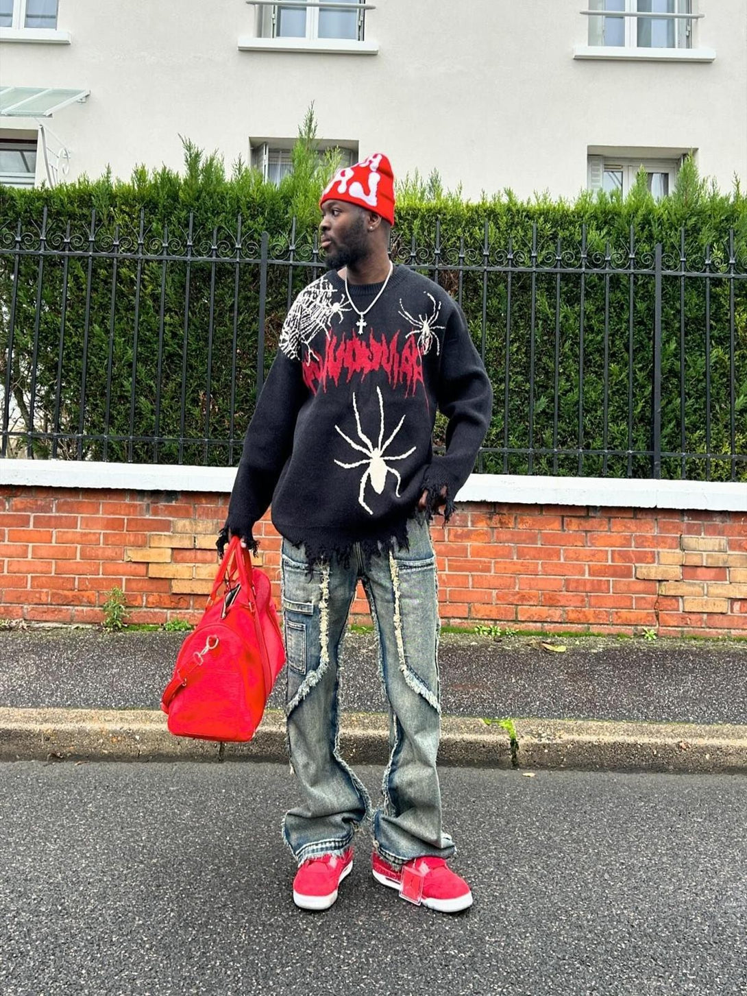 Model wearing TALISHKO's distressed jeans with raw hem, paired with a bold sweater and red accessories.