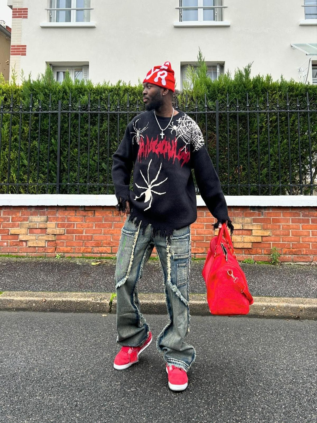 Model in TALISHKO's distressed jeans with raw hems, styled with a graphic sweater and red accents.