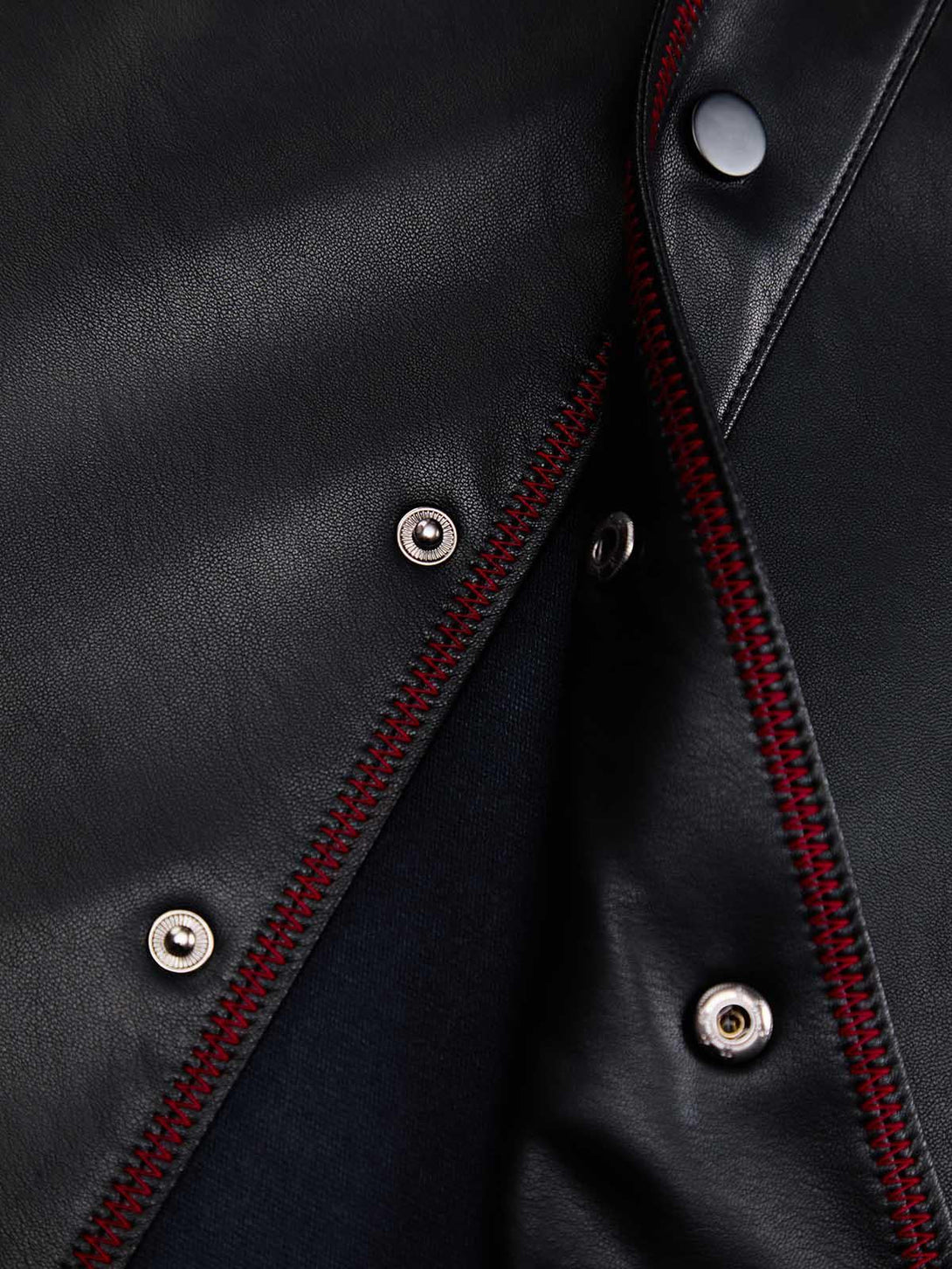 Close-up of TALISHKO's leather shirt with red stitching and metallic snap details.