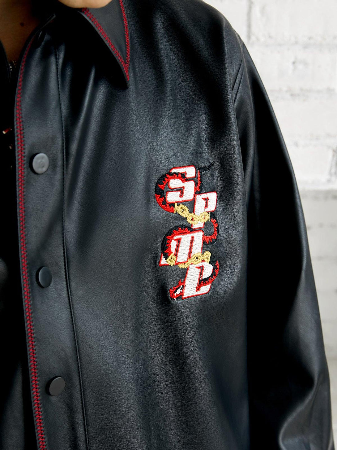 A detailed view of TALISHKO's leather shirt, featuring bold embroidery and red stitching accents.