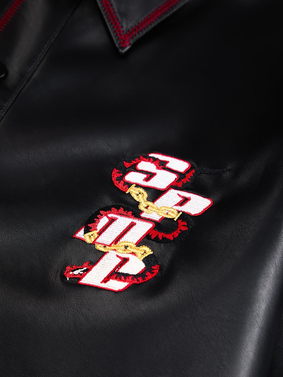 Intricate look at TALISHKO's leather shirt, showcasing bold embroidered details and red stitching.