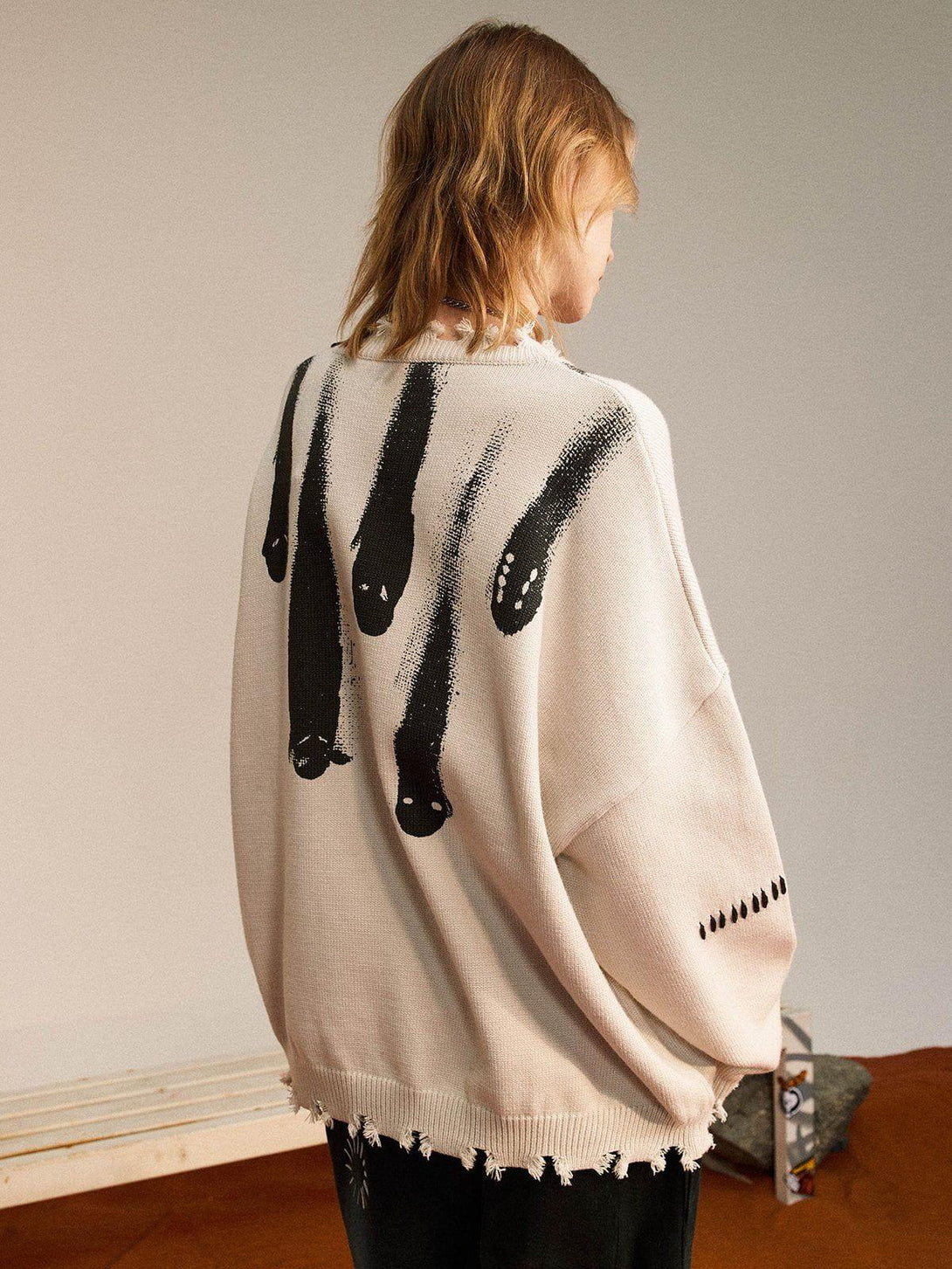 Model in TALISHKO knit sweater featuring abstract black design and frayed hem detailing.