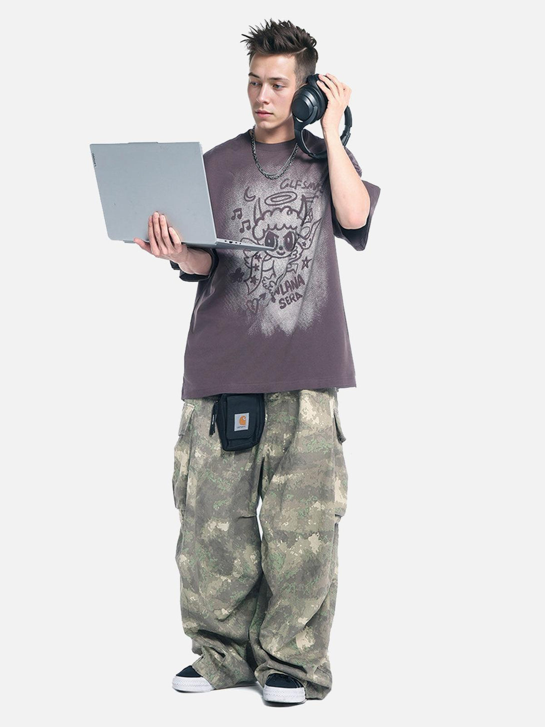 Model wearing TALISHKO oversized angel graphic T-shirt with camo pants and headphones.