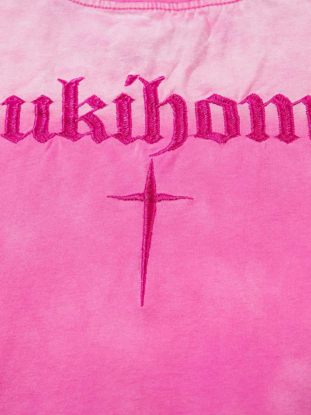 Detailed close-up of TALISHKO pink t-shirt with bold lettering and cross embroidery design.