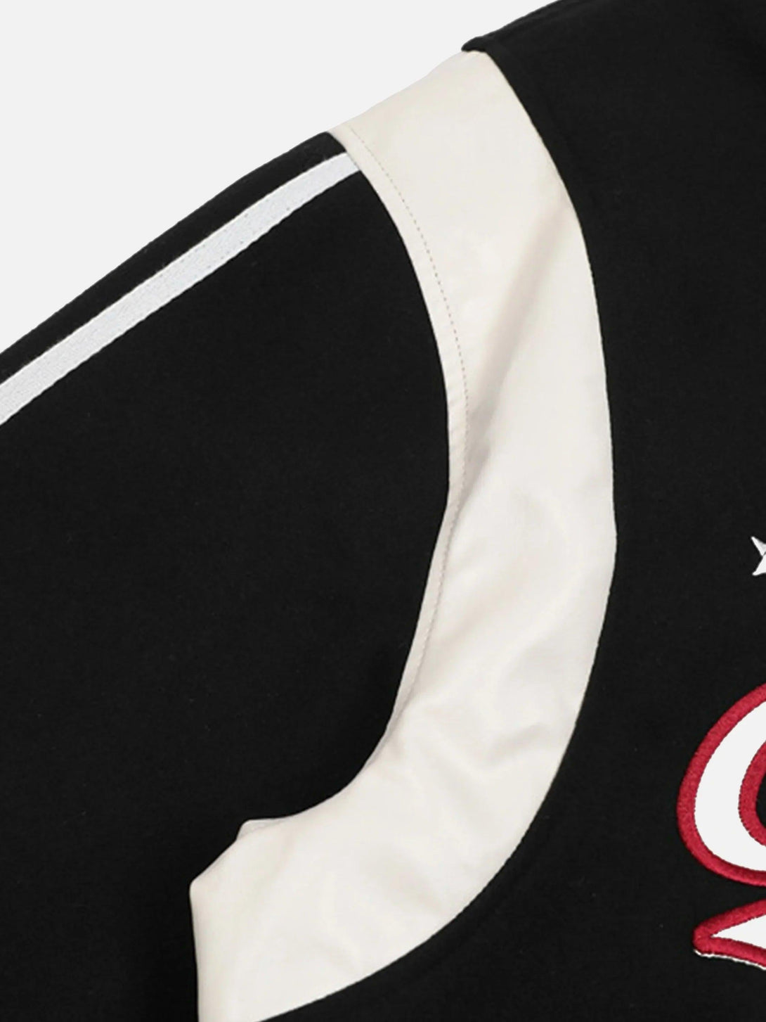 A close-up of TALISHKO's black baseball jacket showcasing contrast stitching and embroidered patchwork.