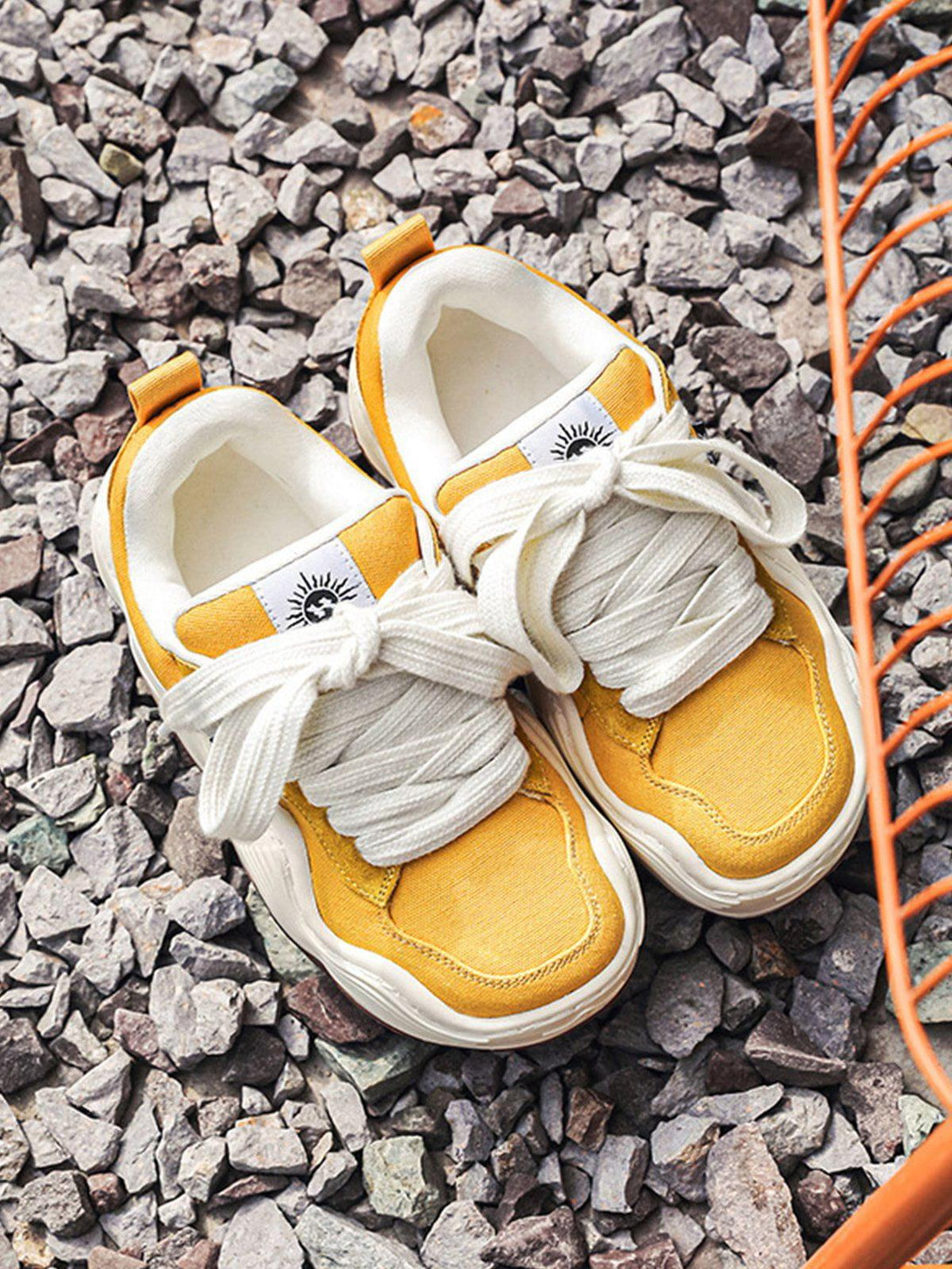 Yellow sneakers with thick white laces by TALISHKO on rocky ground, showcasing casual style.