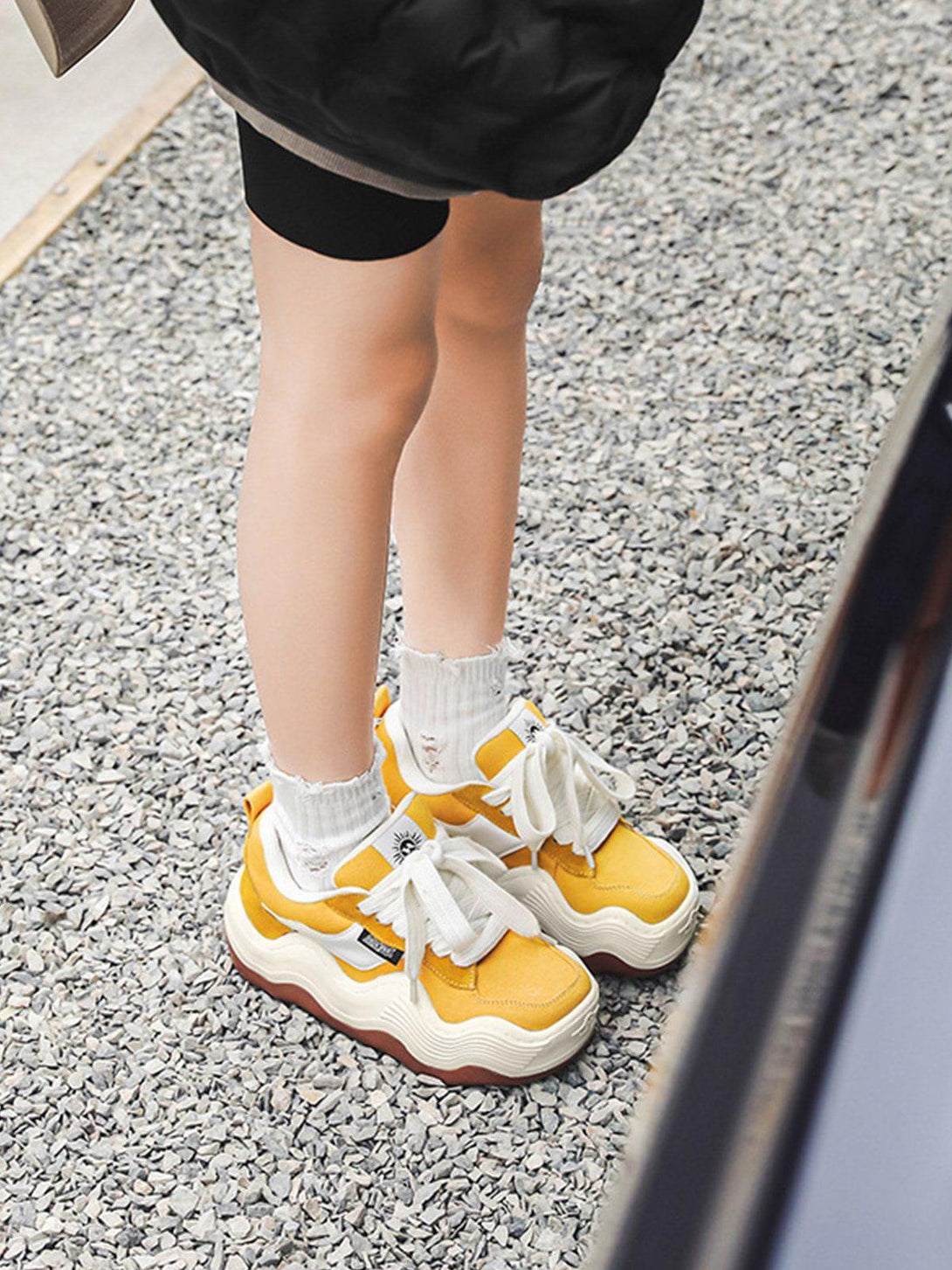 TALISHKO yellow patchwork sneakers with thick wavy soles, styled with white socks on gravel.