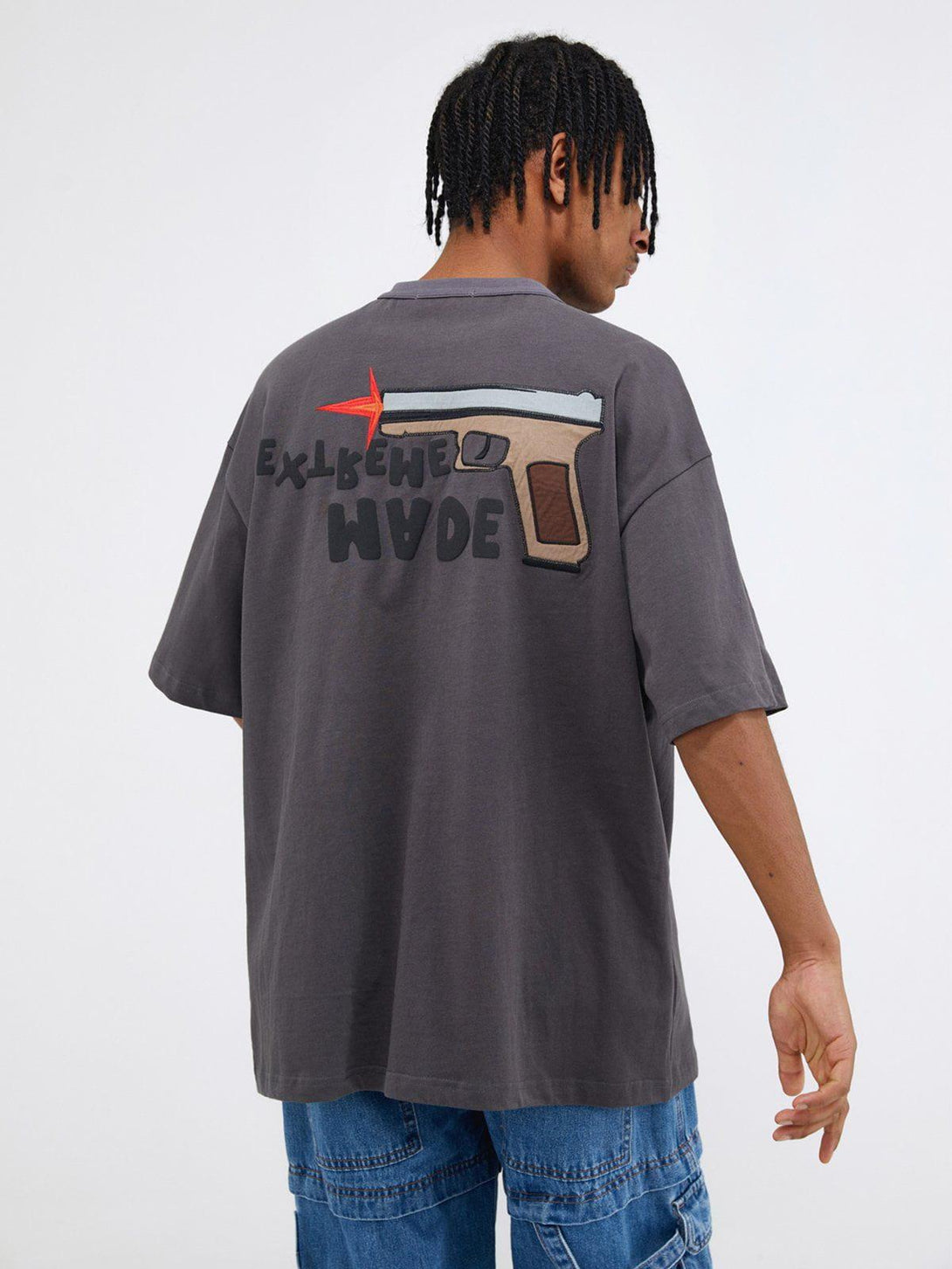 Back view of gray TALISHKO tee with bold pistol graphic and text, worn by model in denim.