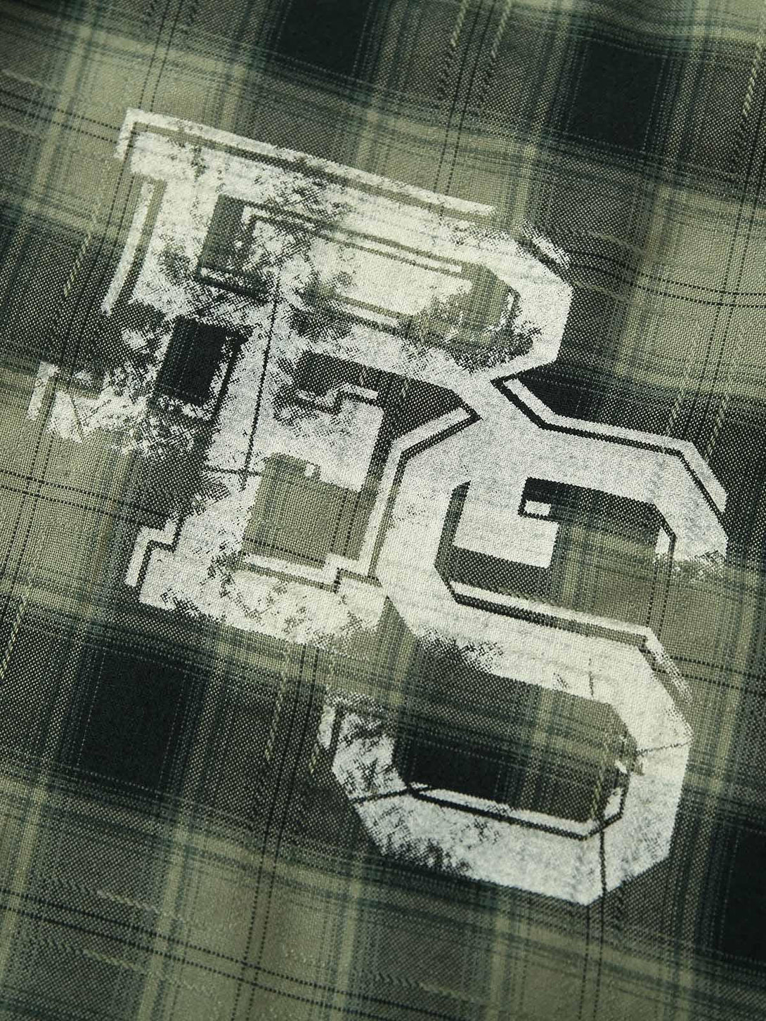 A close-up of TALISHKO's plaid shirt fabric with a bold applique, highlighting texture and design.