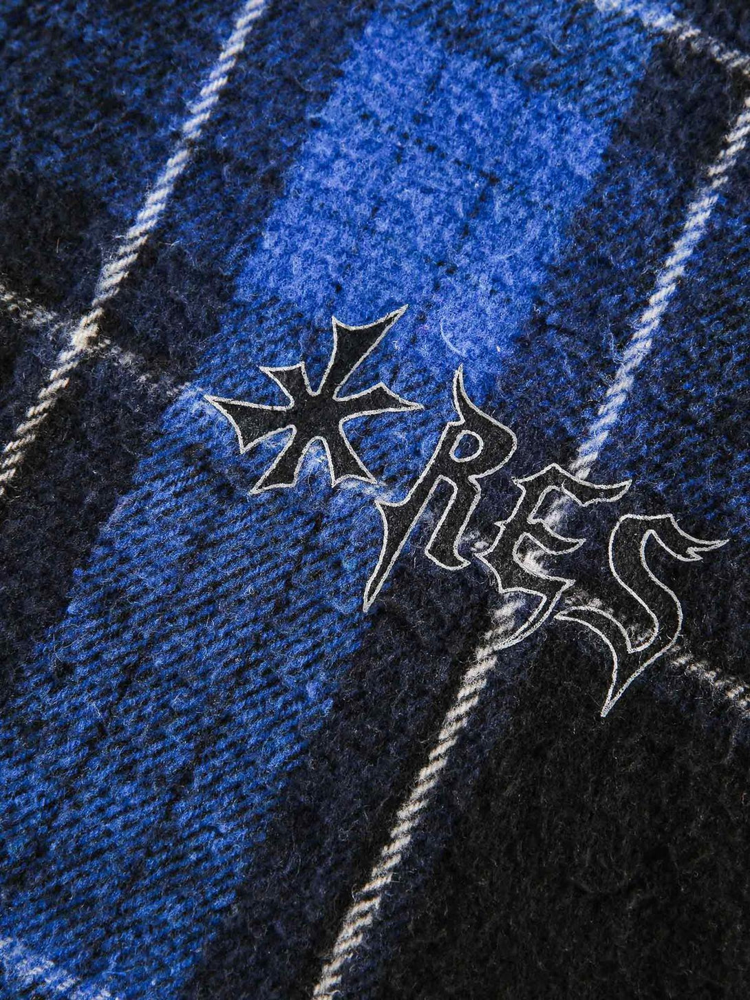 A tight crop highlighting TALISHKO's blue plaid cardigan fabric and unique embroidered design.