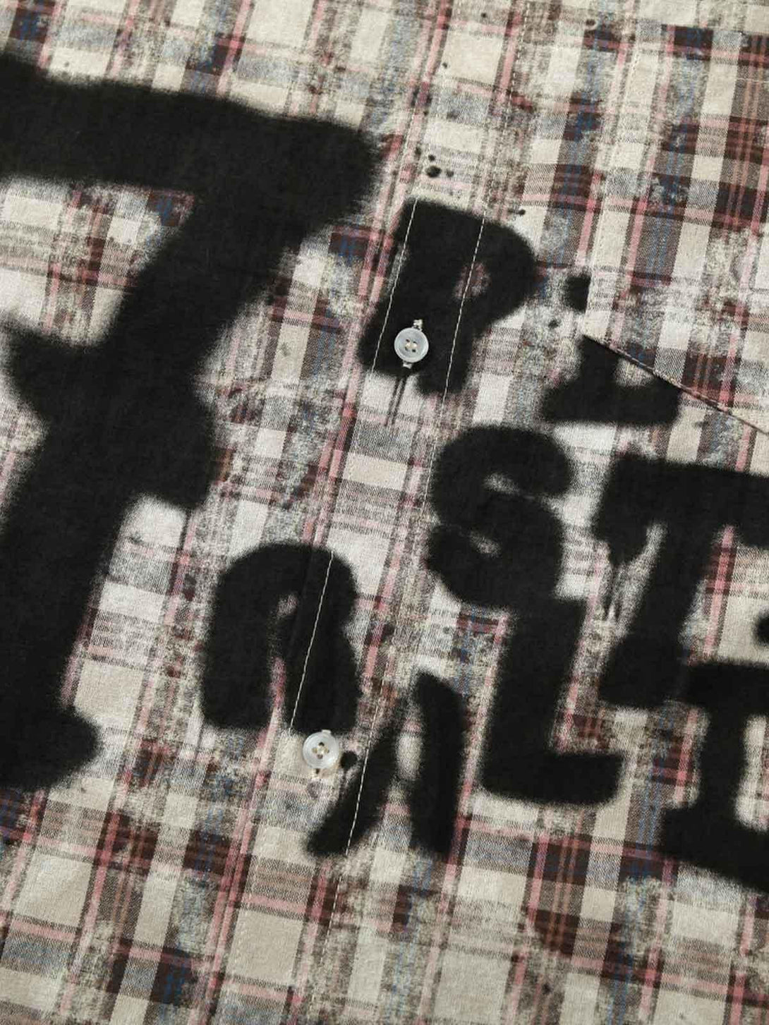Zoomed-in texture of TALISHKO plaid shirt with spray-painted graffiti-style letters.