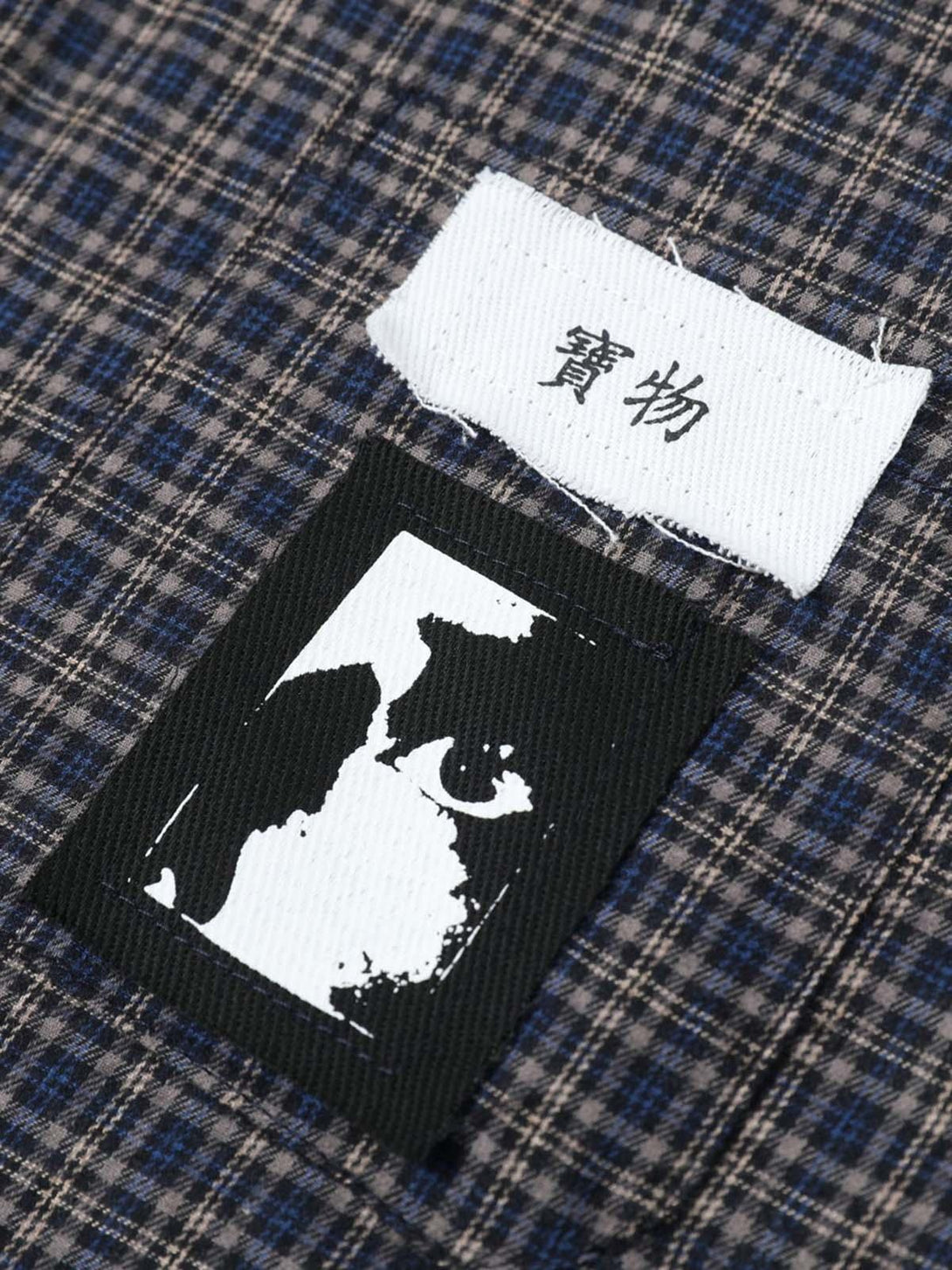 Detailed fabric and stitching on TALISHKO's plaid polo shirt, emphasizing unique patches.