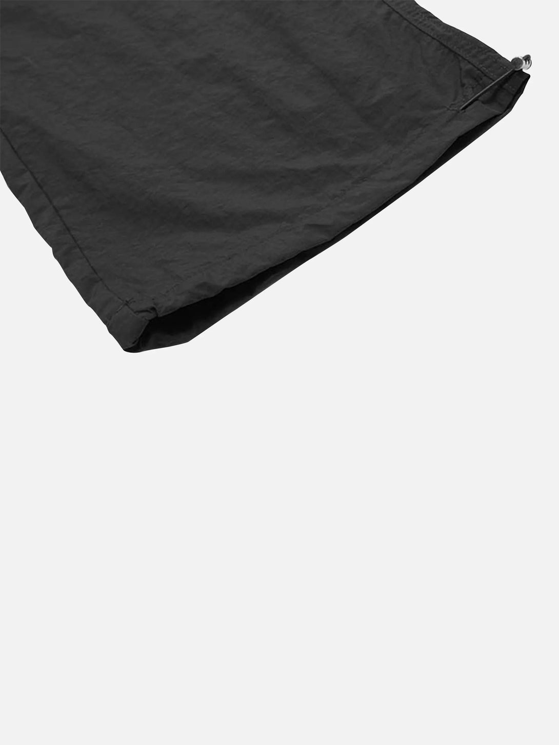 Zoomed-in texture of black TALISHKO cargo pants, highlighting pleated fabric and drawstring detail.