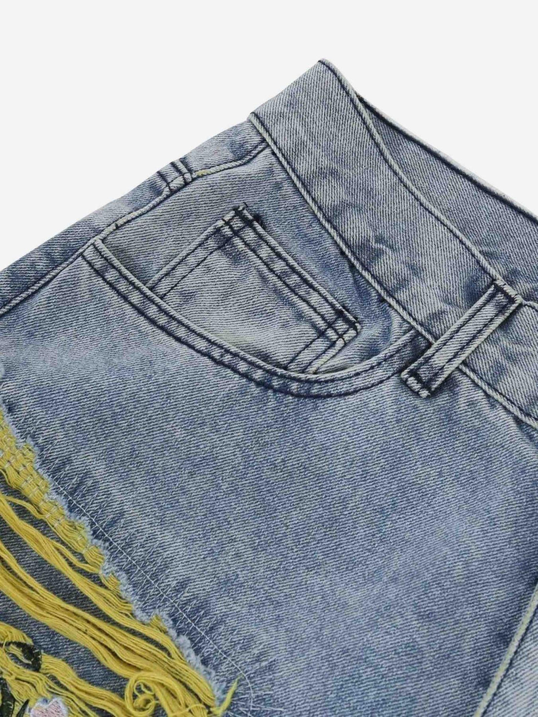 A close-up of TALISHKO jeans highlighting yellow distressing and intricate embroidery detail.