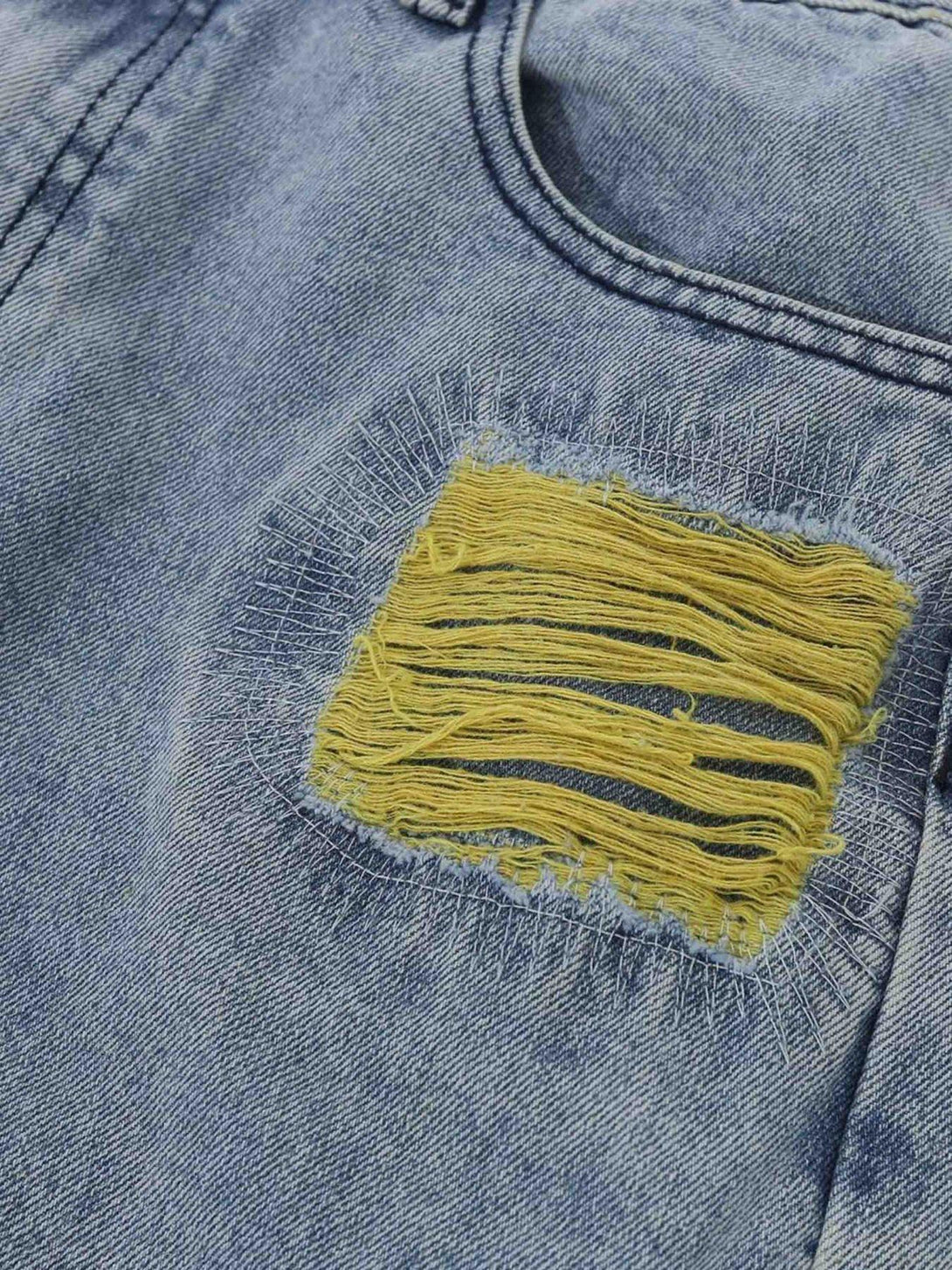 Detailed fabric and stitching of TALISHKO jeans with yellow distressing and unique embroidery.