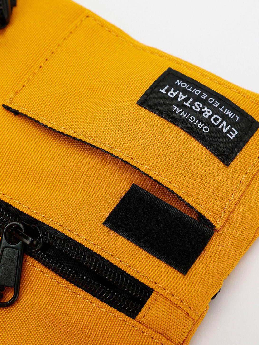 A detailed view of the TALISHKO yellow crossbody bag, highlighting the black zipper and patch.