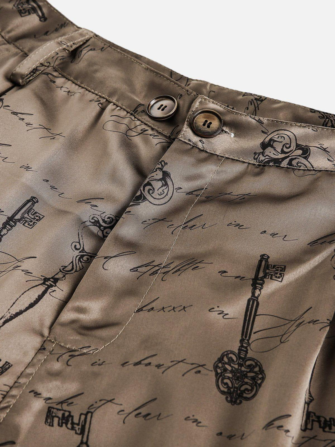 Intricate look at TALISHKO silk shorts, highlighting vintage key and script design details.