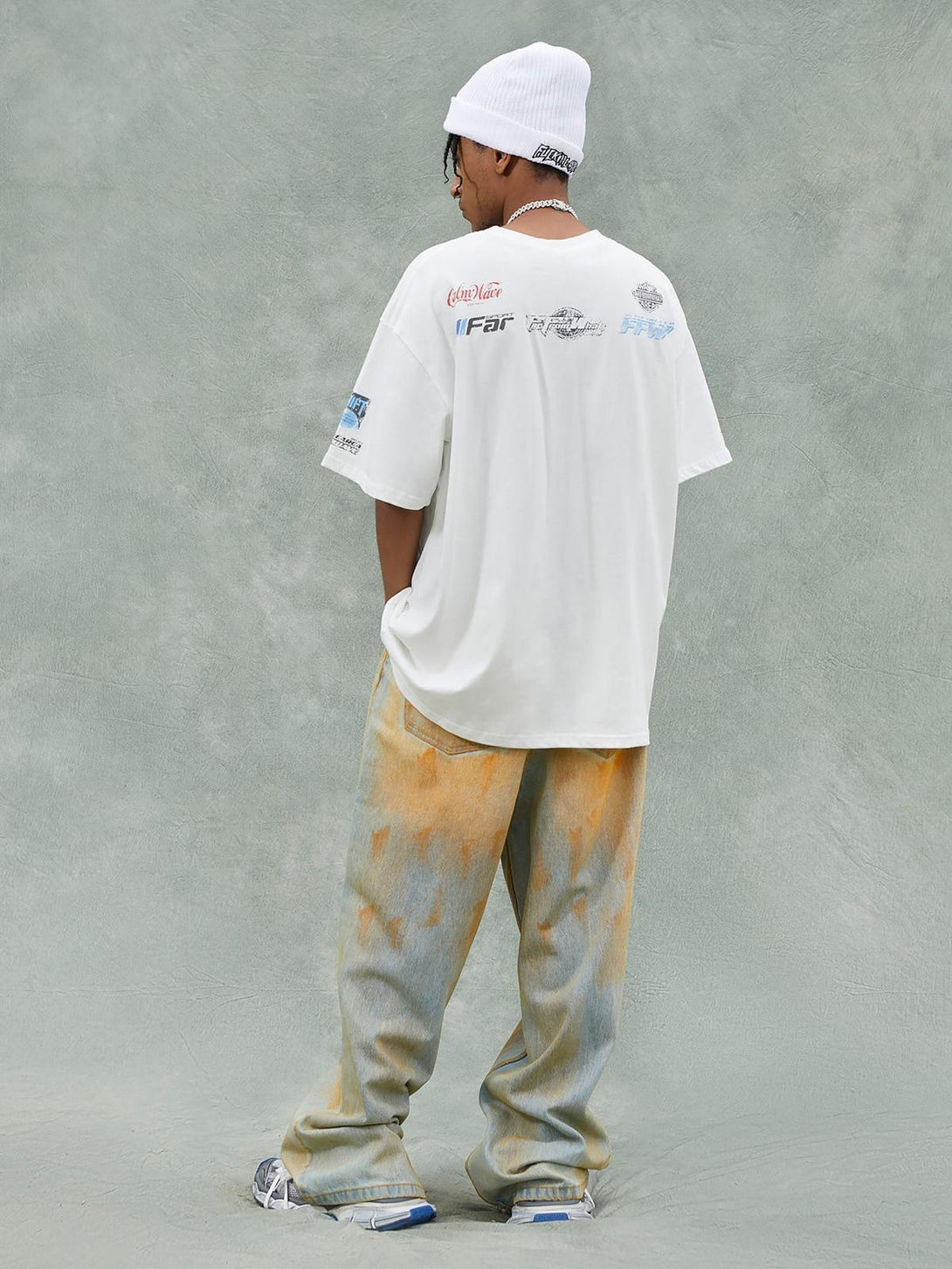 Model wearing a TALISHKO T-shirt with graphic back design, paired with distressed denim.