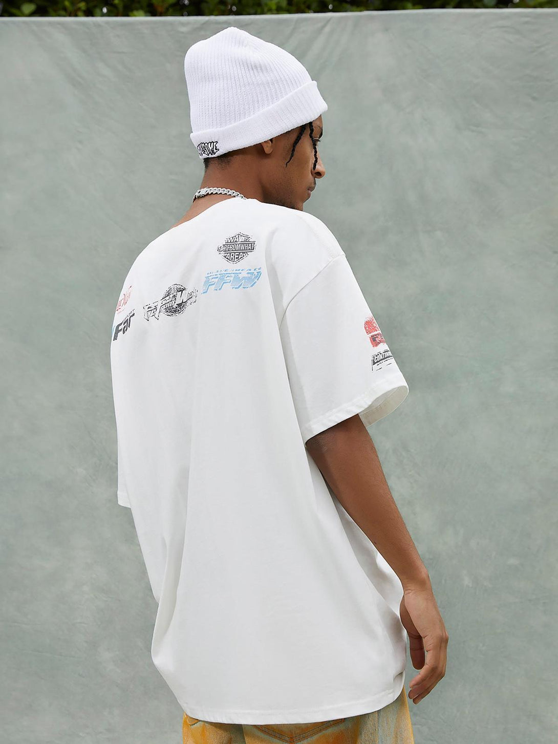 Model in a TALISHKO T-shirt with graphic back design, paired with a white beanie for a casual look.