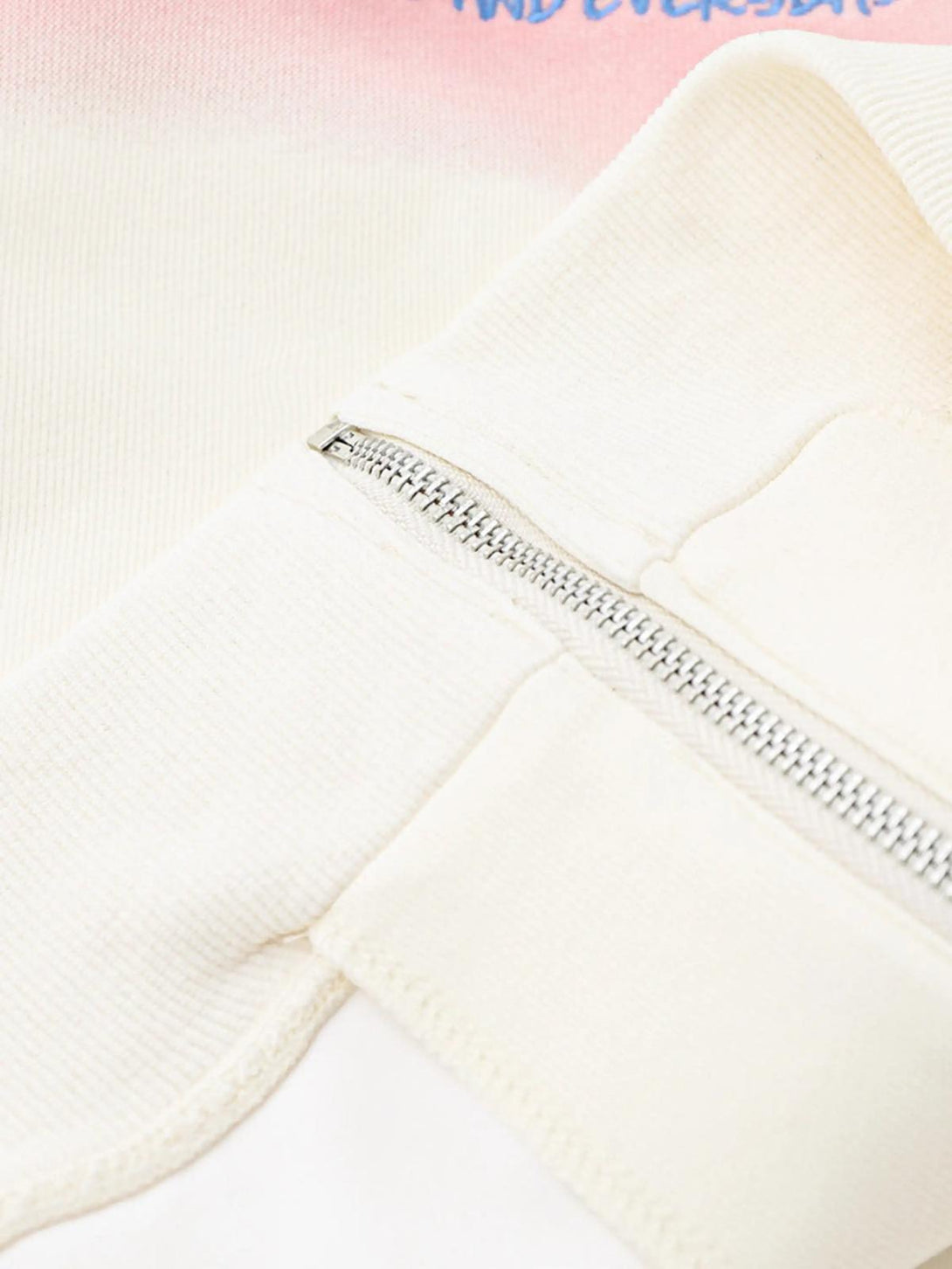 A close-up of a TALISHKO hoodie zipper detail, featuring a soft blend of pastel pink and cream.