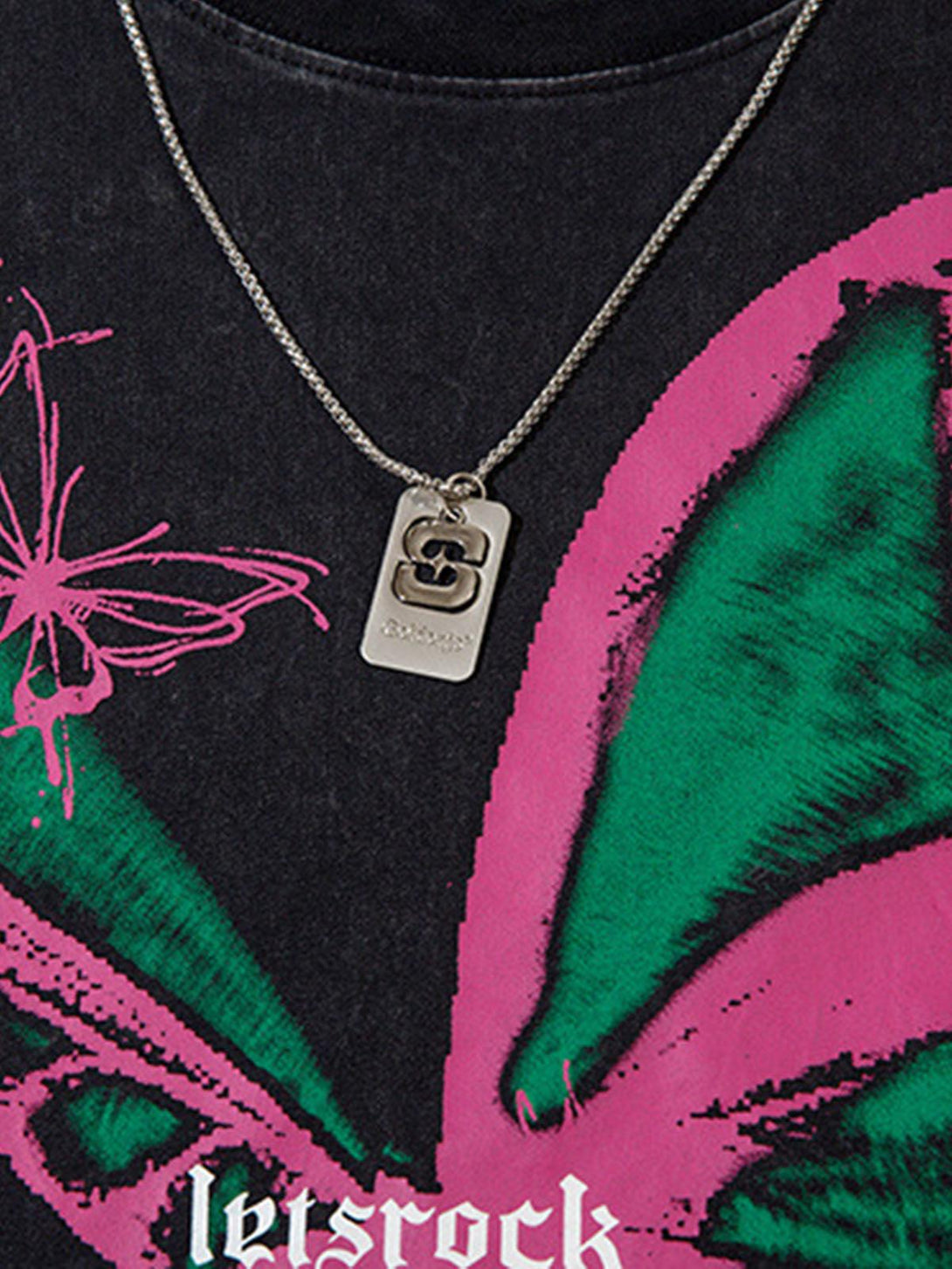 A close-up of a TALISHKO necklace on a butterfly print vest, showcasing unique design elements.