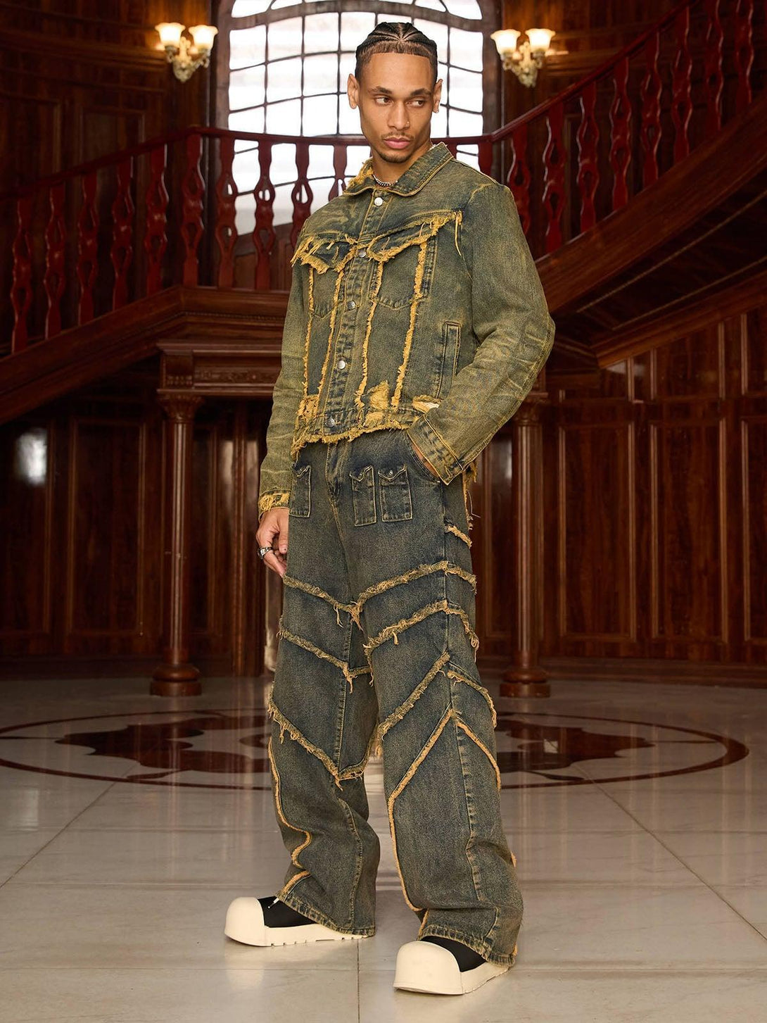 Model in TALISHKO's raw edge distressed denim jacket, styled with matching pants in a grand setting.