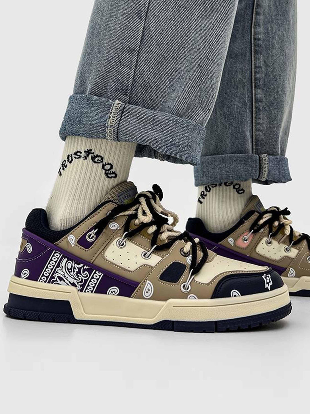 TALISHKO sneakers in beige and purple with paisley accents, paired with rolled-up denim jeans.