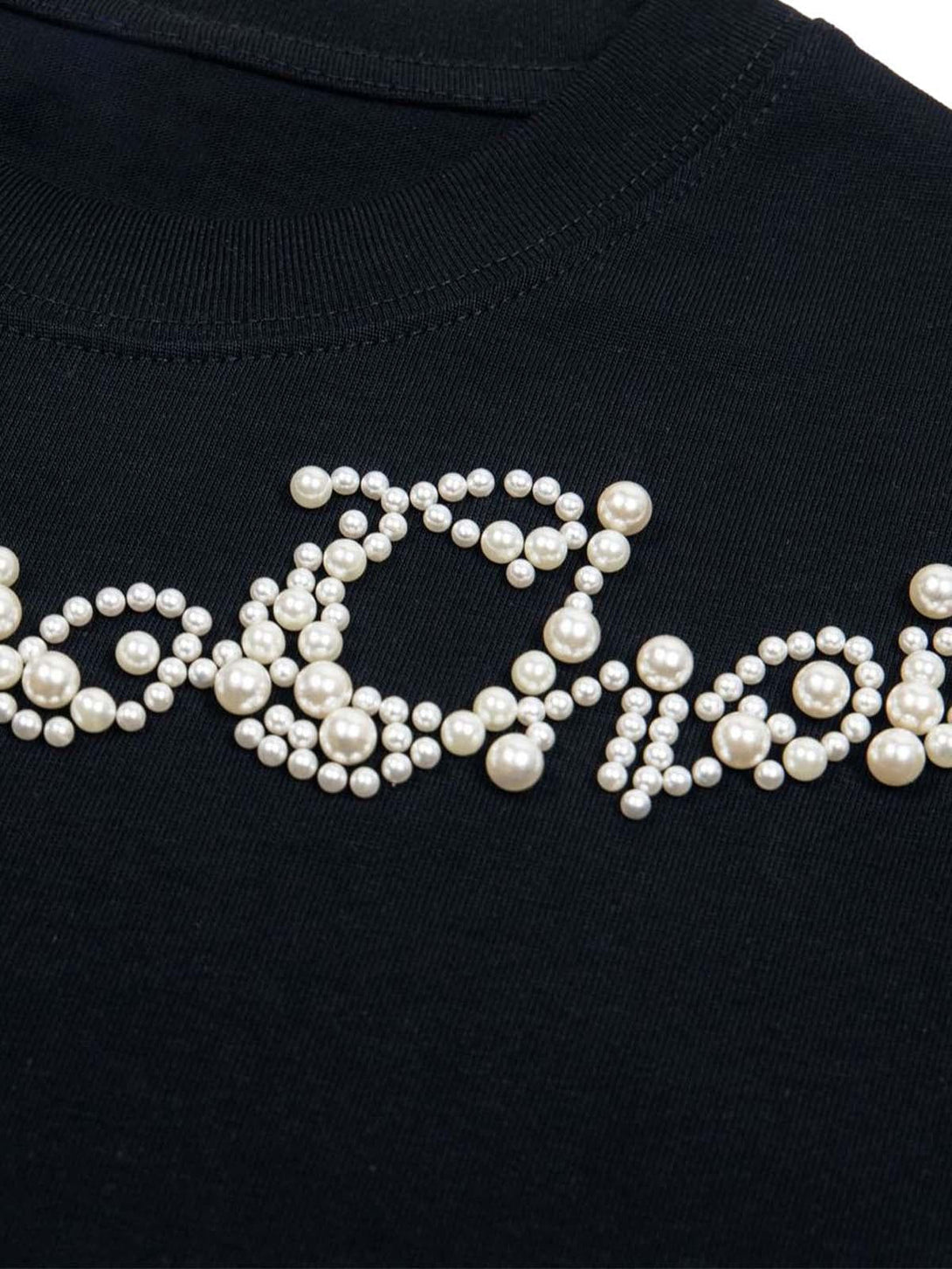 Intricate view of pearl-beaded lettering on a black T-shirt by TALISHKO, showcasing unique style.