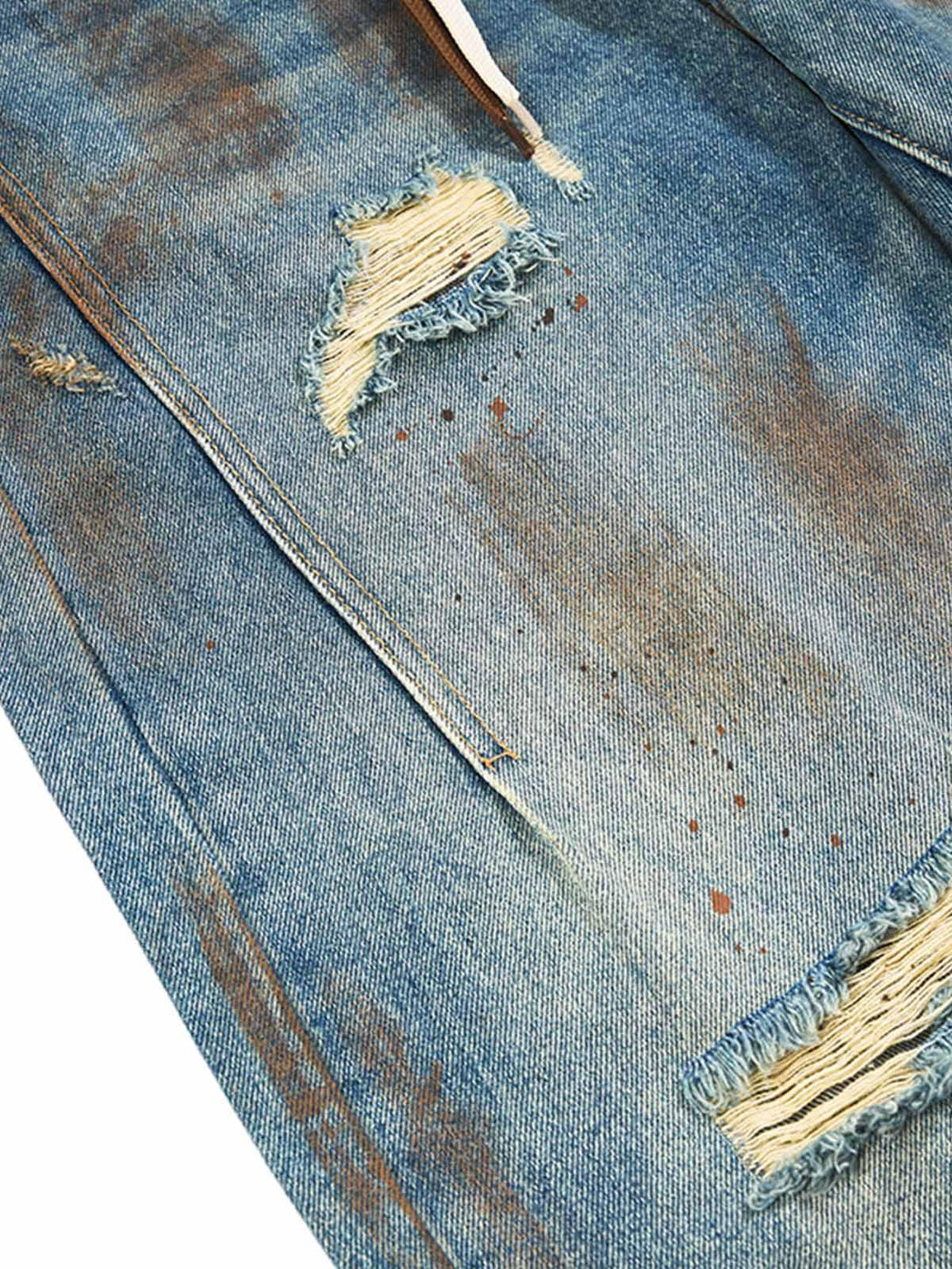 A tight crop highlighting the distressed texture of TALISHKO retro ink-splashed ripped jeans.