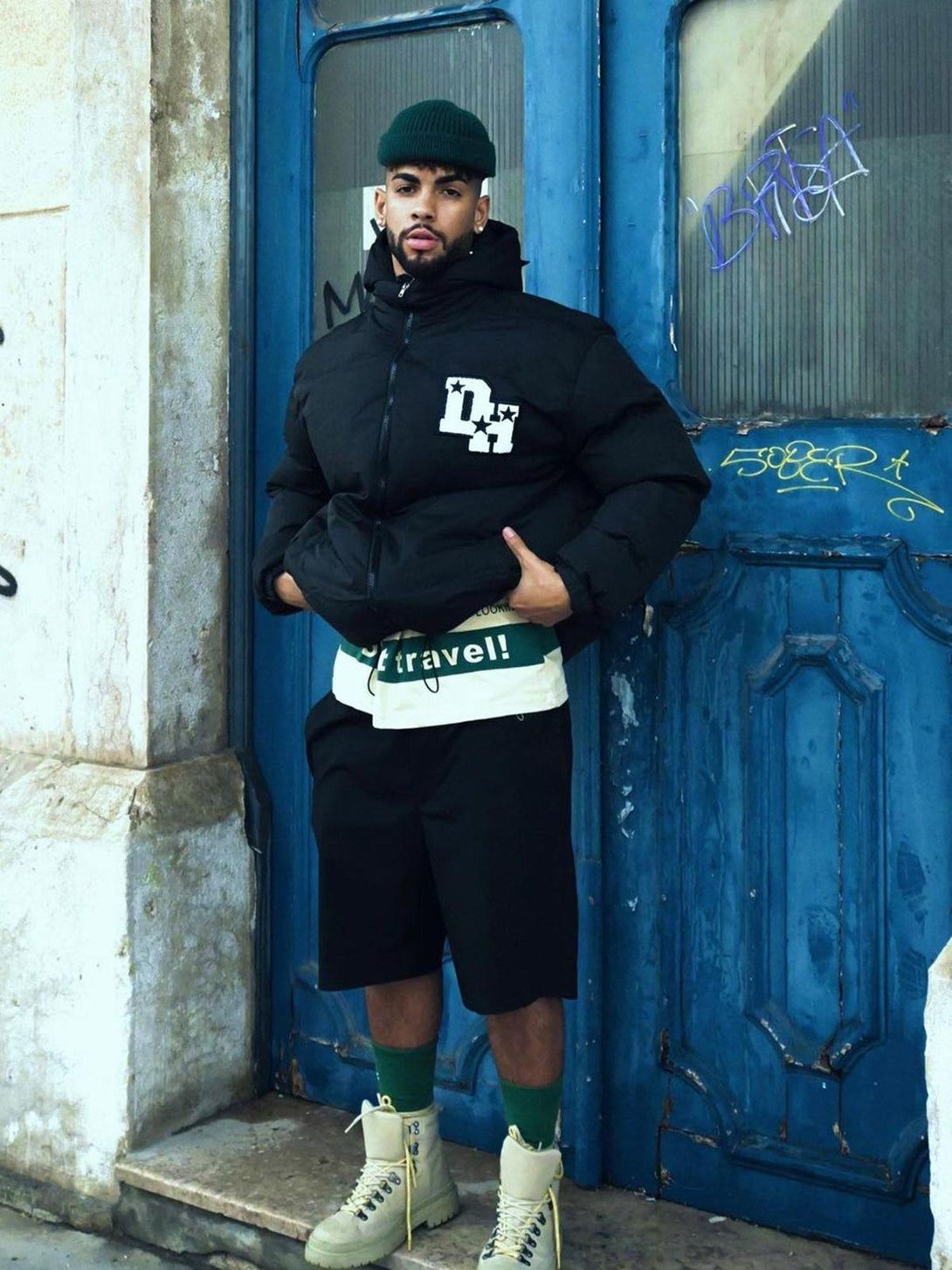 Model wearing TALISHKO black down jacket with retro letter print, paired with shorts and boots.