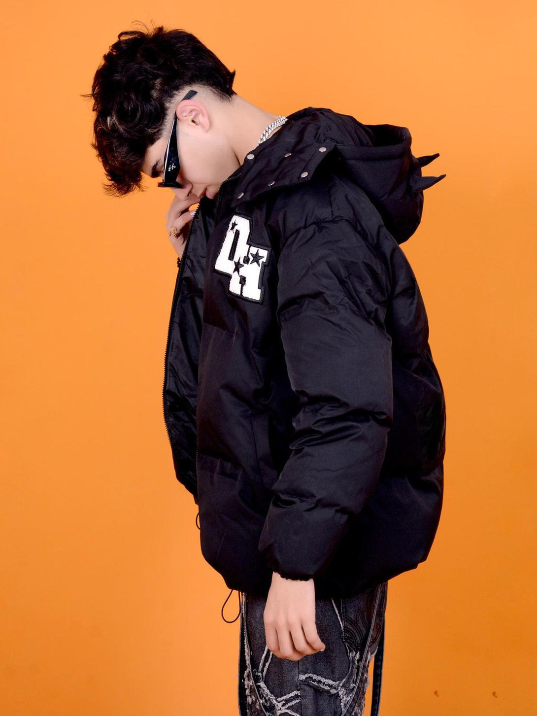 Model in TALISHKO black down jacket with retro letter print and star accent on orange backdrop.