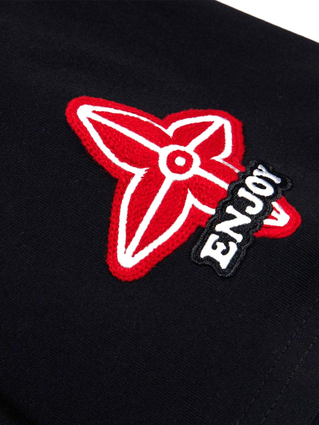 A detailed view of the TALISHKO T-shirt showcasing bold red embroidery and retro patches.