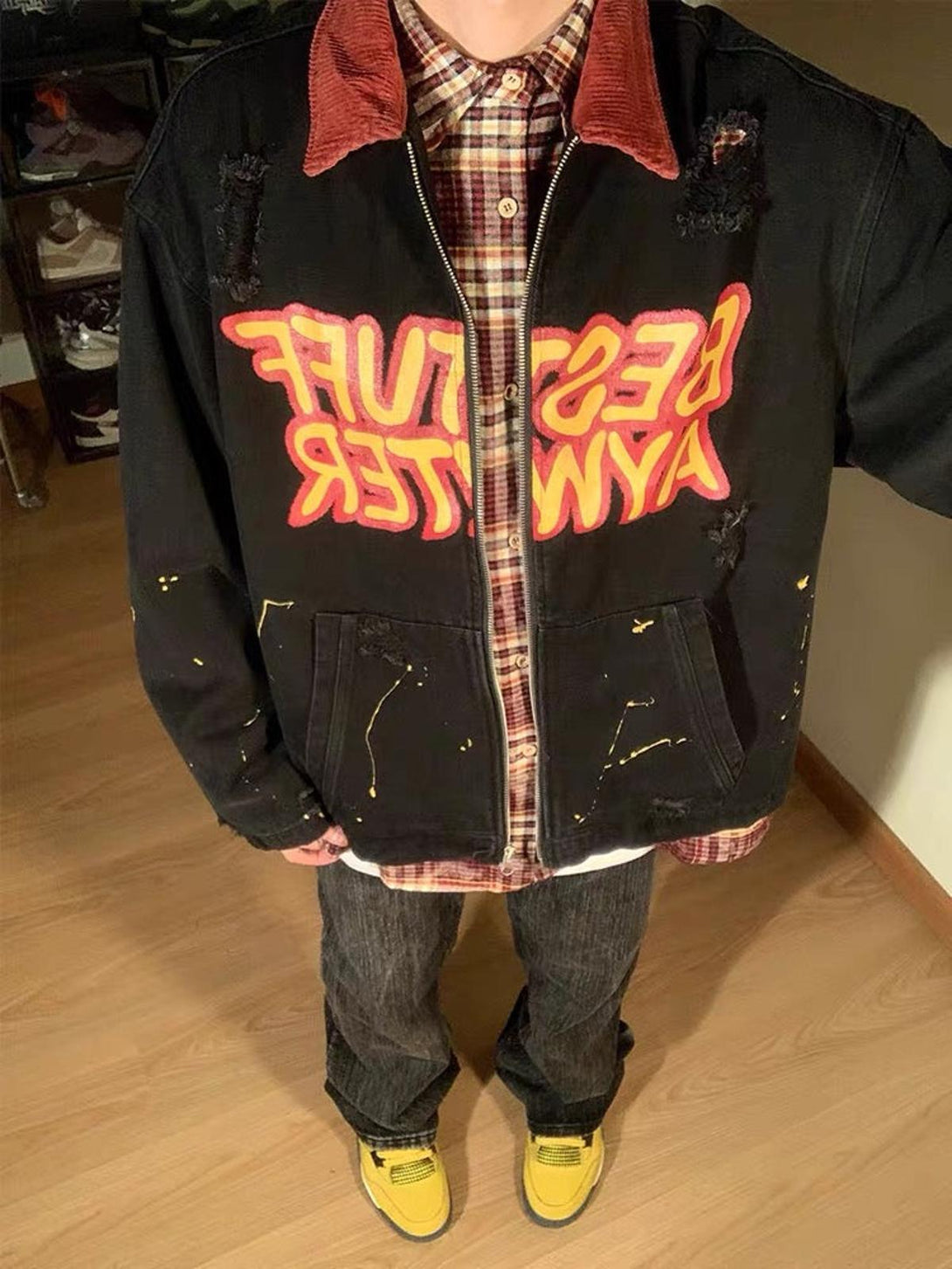 Model showcasing TALISHKO's retro patchwork denim jacket with bold lettering and plaid shirt.