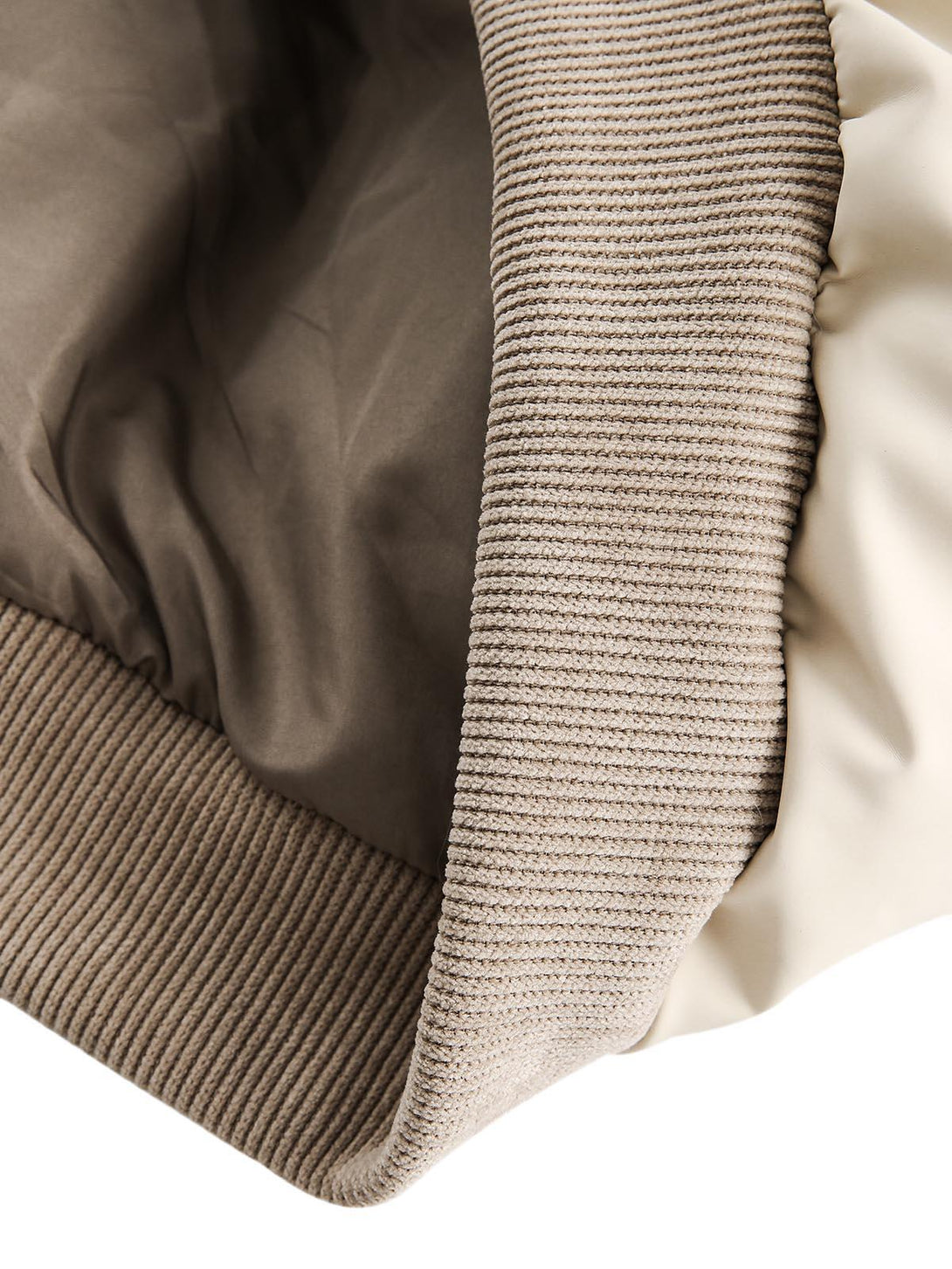 A tight crop highlighting the ribbed hem and lining detail of TALISHKO's puffer bomber jacket.