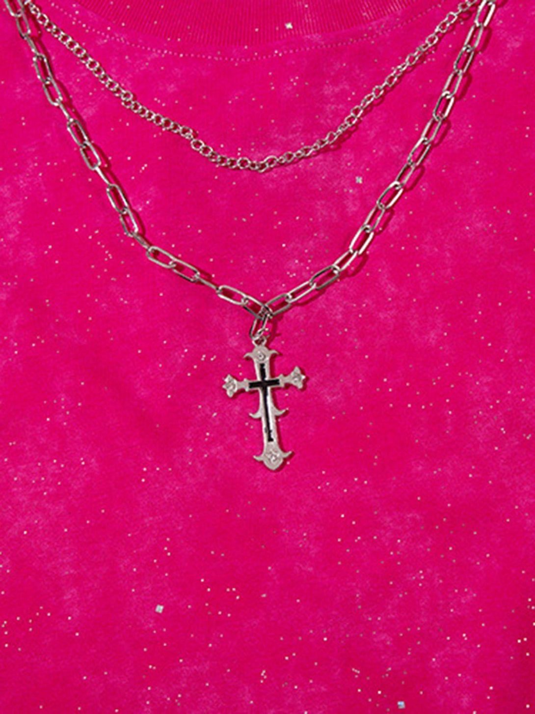 A close-up of TALISHKO's cross chain detail on a vibrant pink sparkly backdrop.