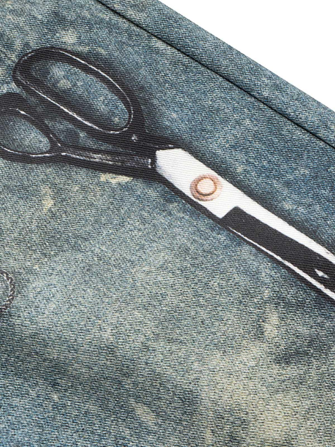 A close-up of TALISHKO's denim shorts showcasing the retro scissors print and textured fabric.