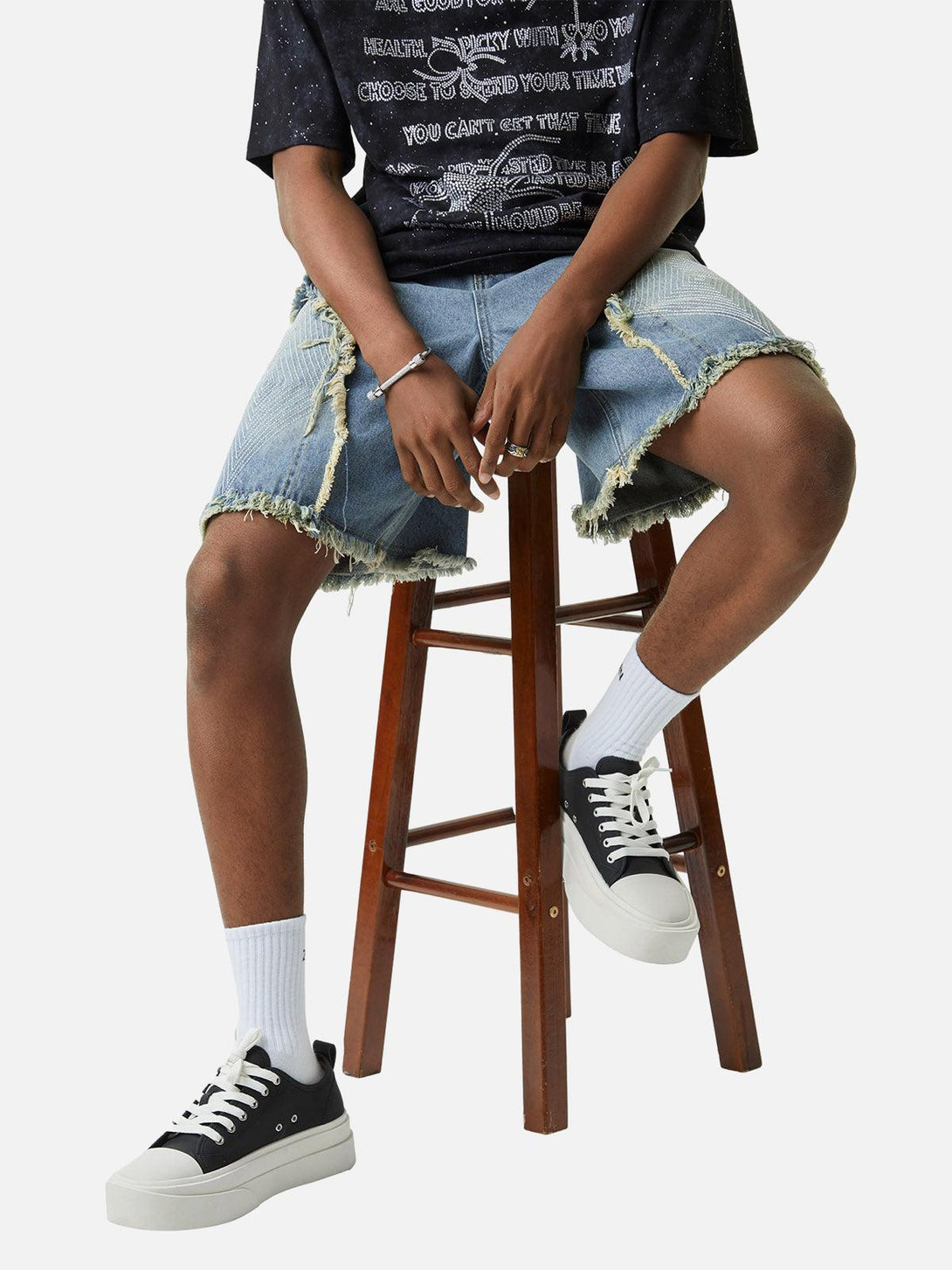 Model sitting on stool in TALISHKO denim shorts, showcasing frayed hems and casual style.
