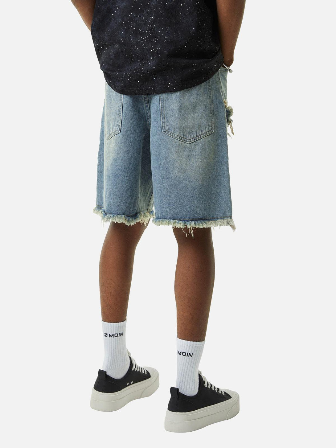 Back view of TALISHKO denim shorts with frayed edges, paired with black sneakers for a relaxed look.