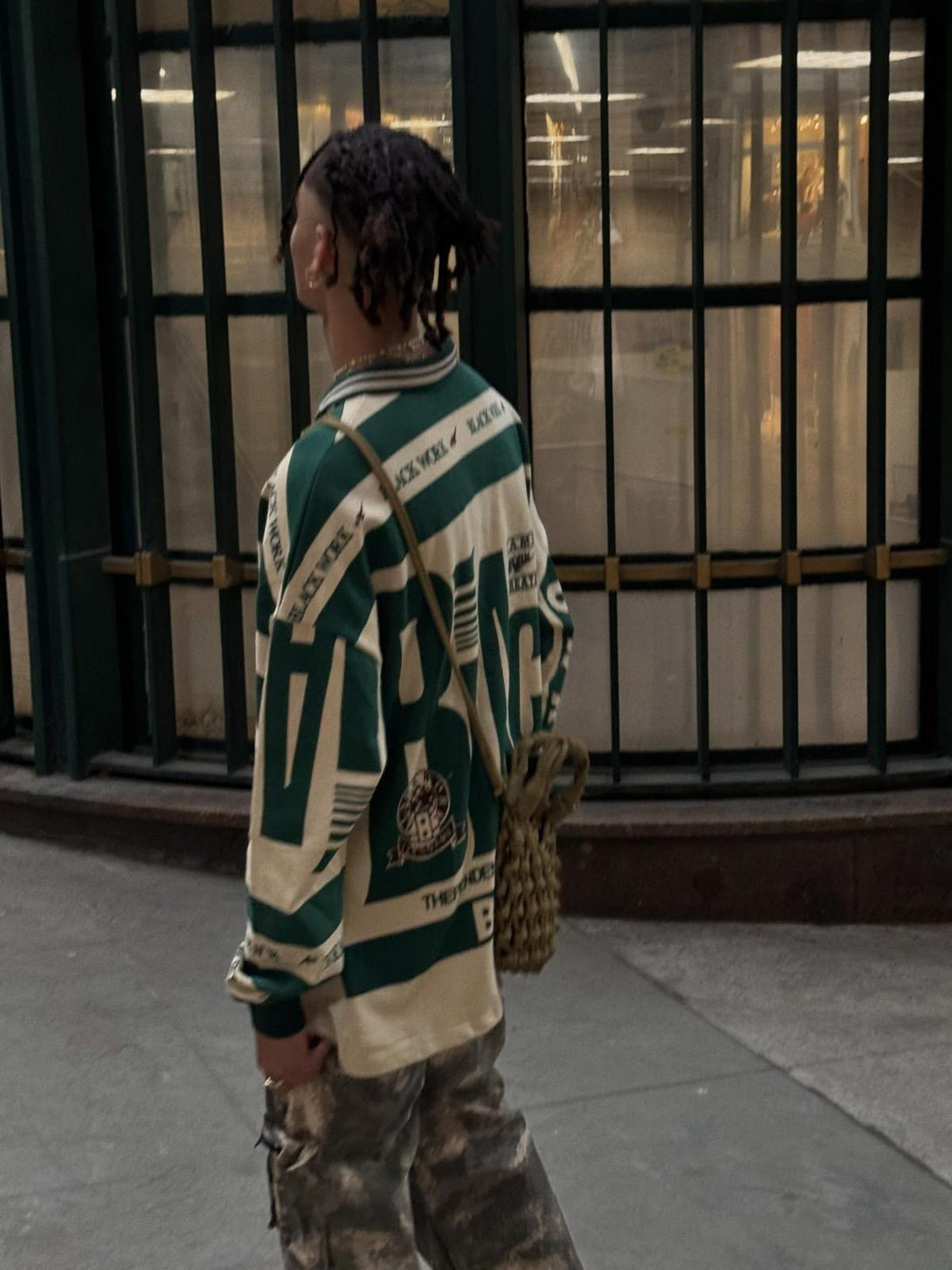 Model in a TALISHKO retro typography polo tee, paired with camo cargo pants and braided bag.
