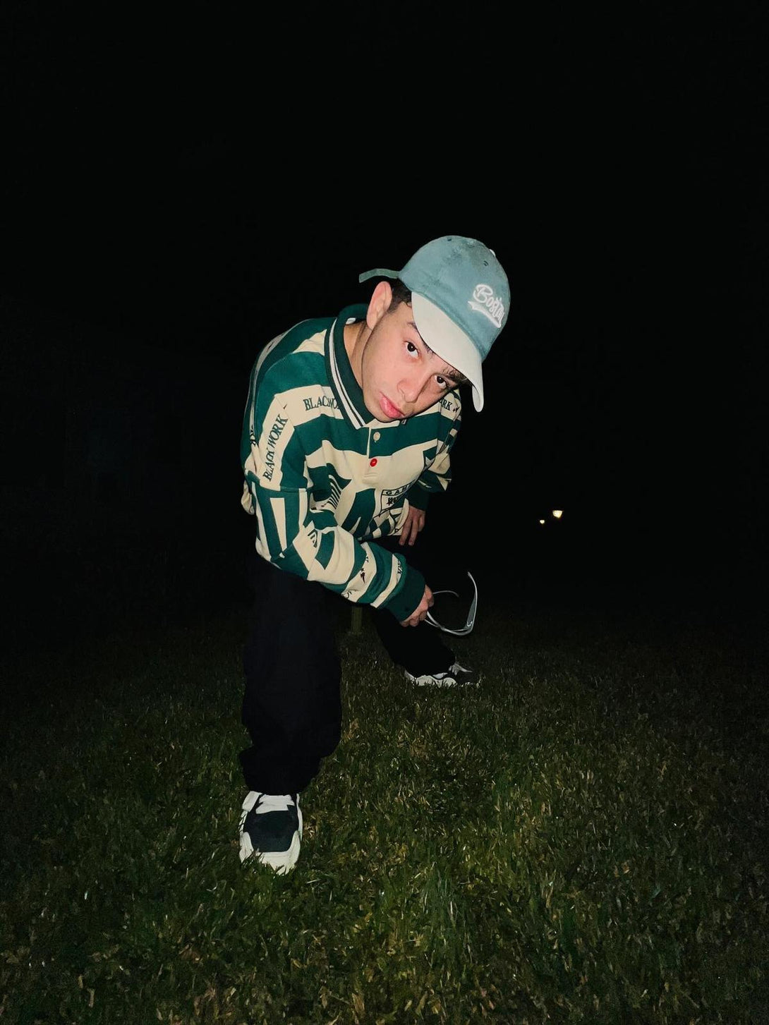 Model crouching in a TALISHKO retro typography polo tee, paired with casual sneakers outdoors.