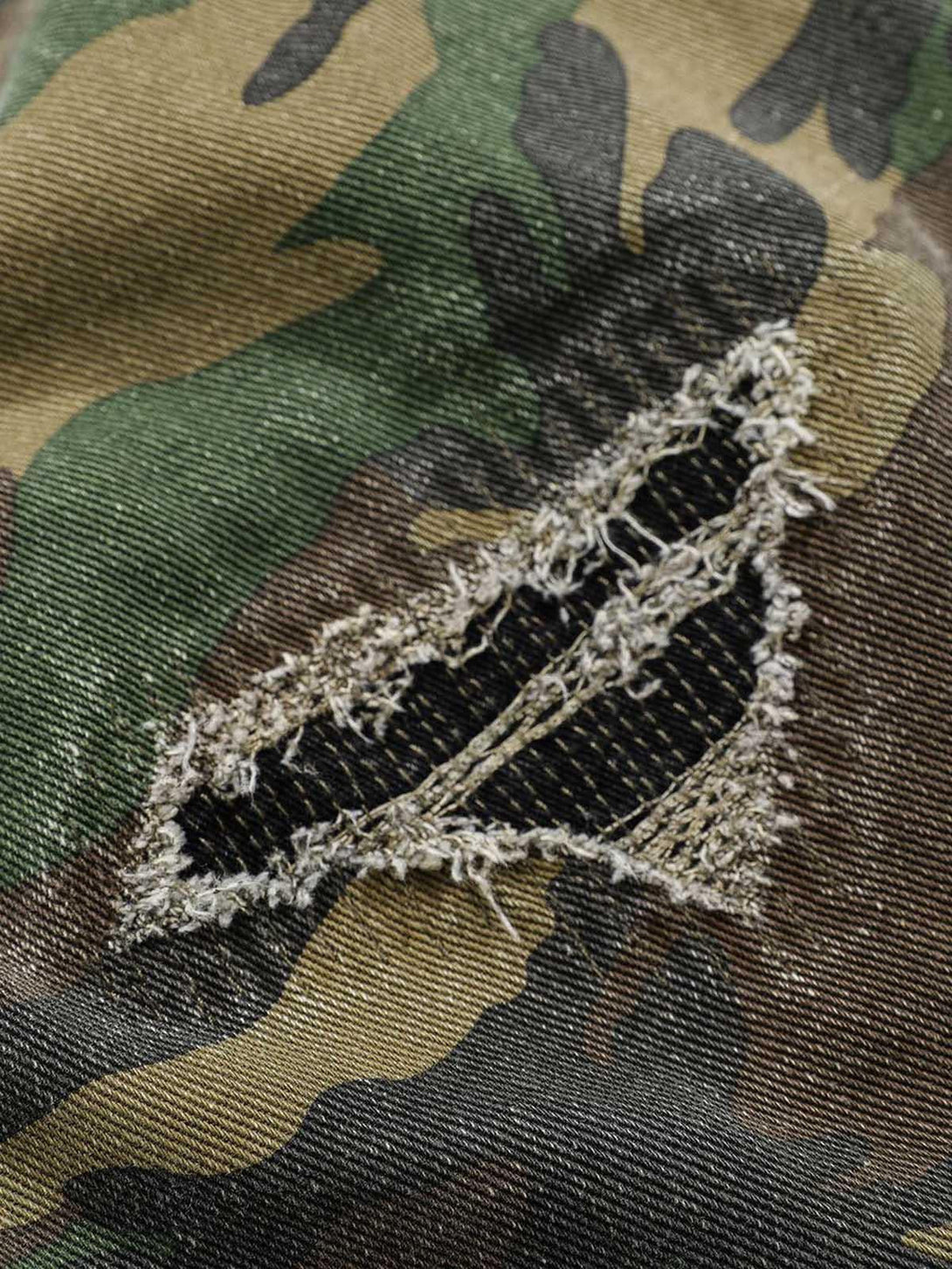 A detailed view of the rugged texture and ripped design on TALISHKO camouflage cargo pants.