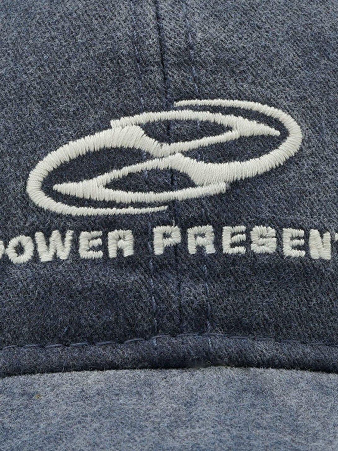 A close-up of a blue denim baseball cap by TALISHKO, highlighting embroidered logo details.