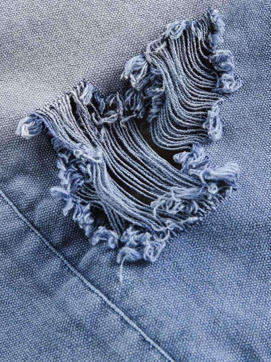 A close-up of distressed denim fabric by TALISHKO, highlighting intricate frayed details.