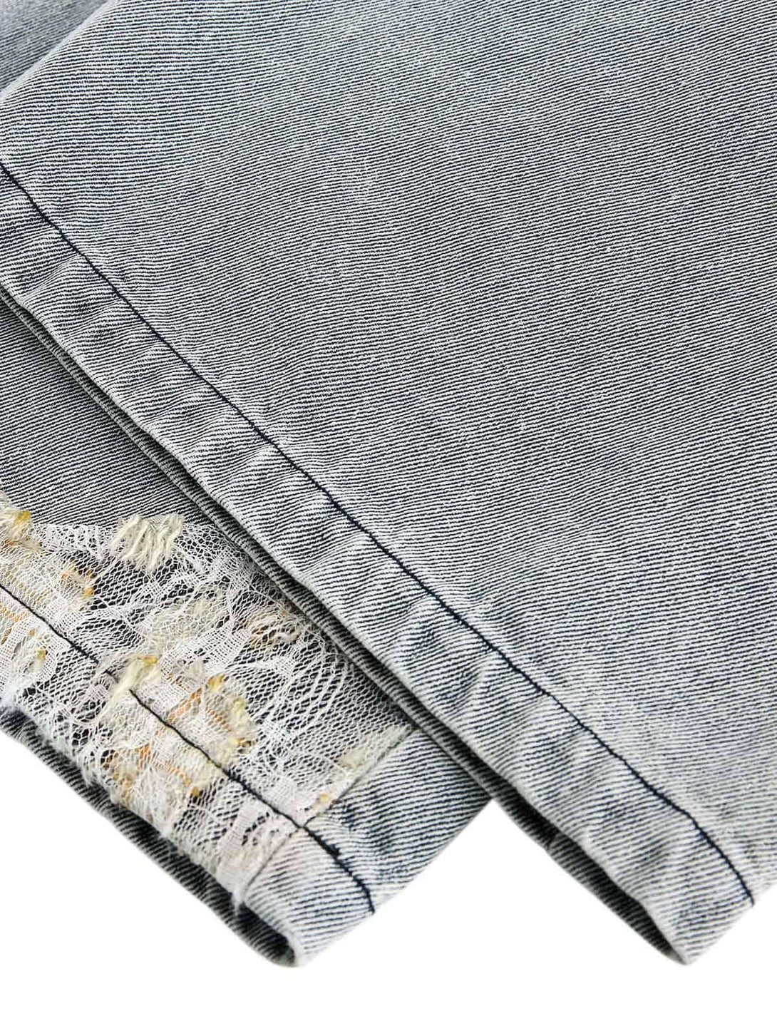 A detailed view of TALISHKO's ripped lace panel denim pants, highlighting unique stitching.