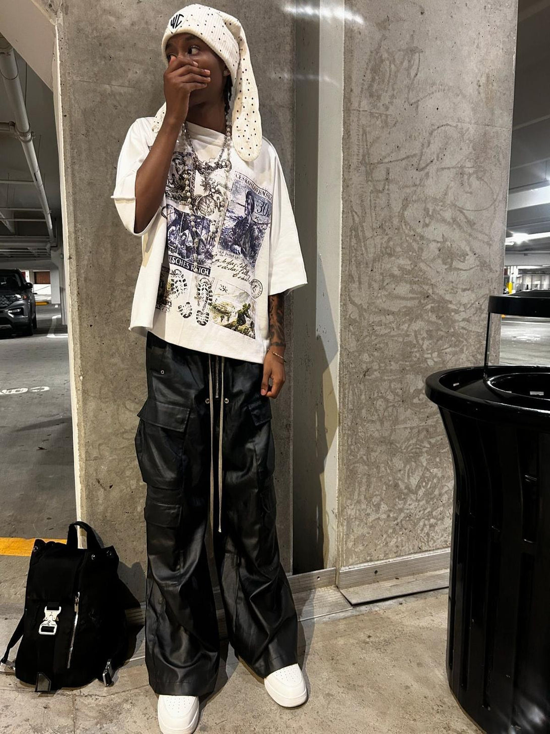 Model in TALISHKO matte coated overalls with multi-pocket design, styled with a graphic tee.
